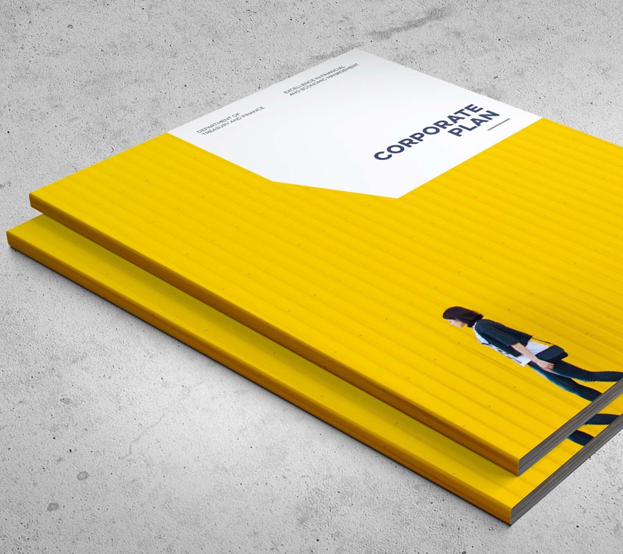 Two yellow hardcover books stacked with the top book titled 'CORPORATE PLAN,' placed on a light gray textured surface. The books have a person walking along the bottom of the cover, a small woman in business attire in front of a big yellow wall.