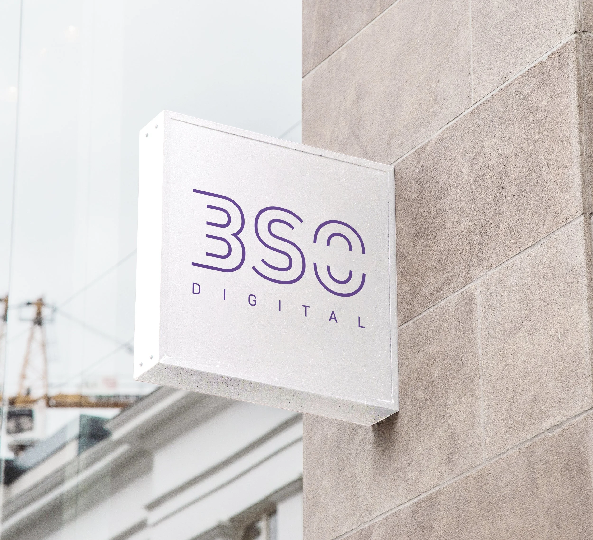 Close-up of a white sign with purple text against a beige brick wall, part of a building exterior.