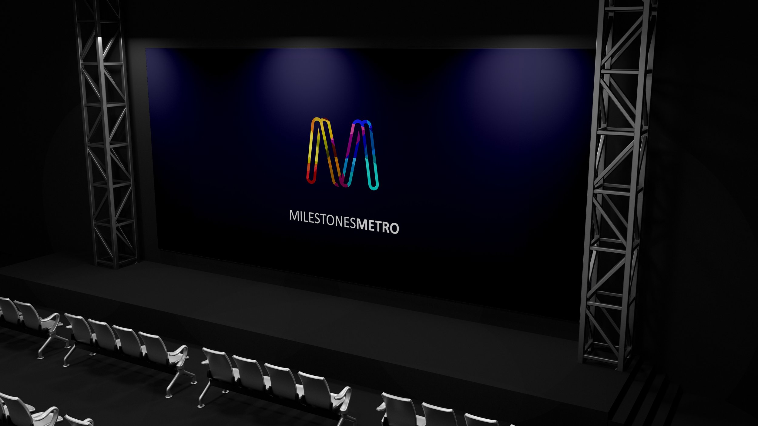 A large stage set up with a dark backdrop featuring a colorful 'M' logo and the text 'MilestonesMetro' beneath it, surrounded by metal trusses and chairs in the foreground.