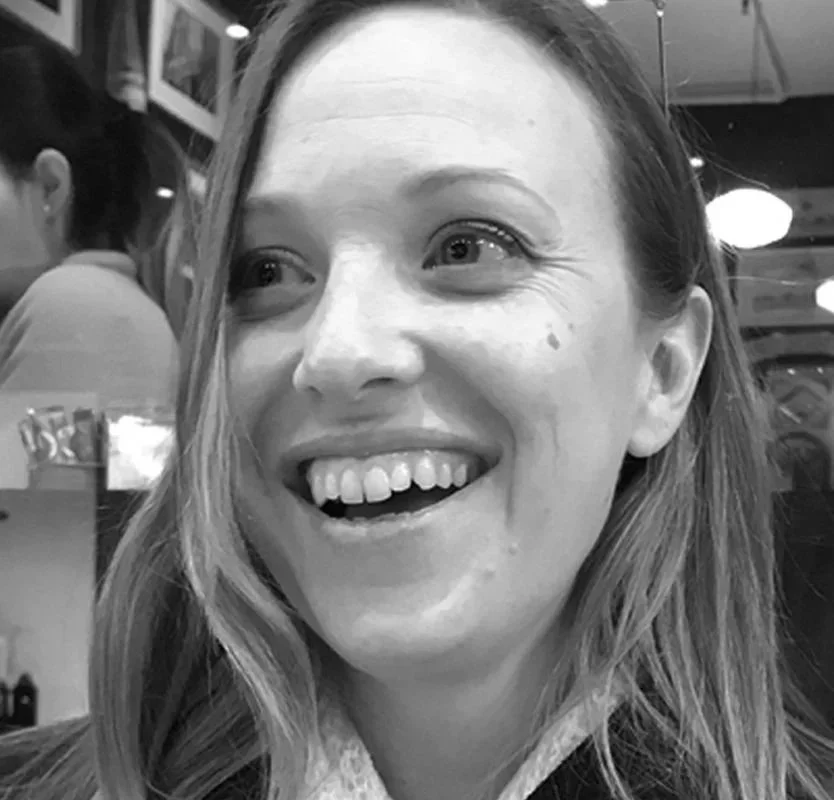 Close-up of a woman with a joyful expression, smiling and showing her teeth, in a lively indoor setting.