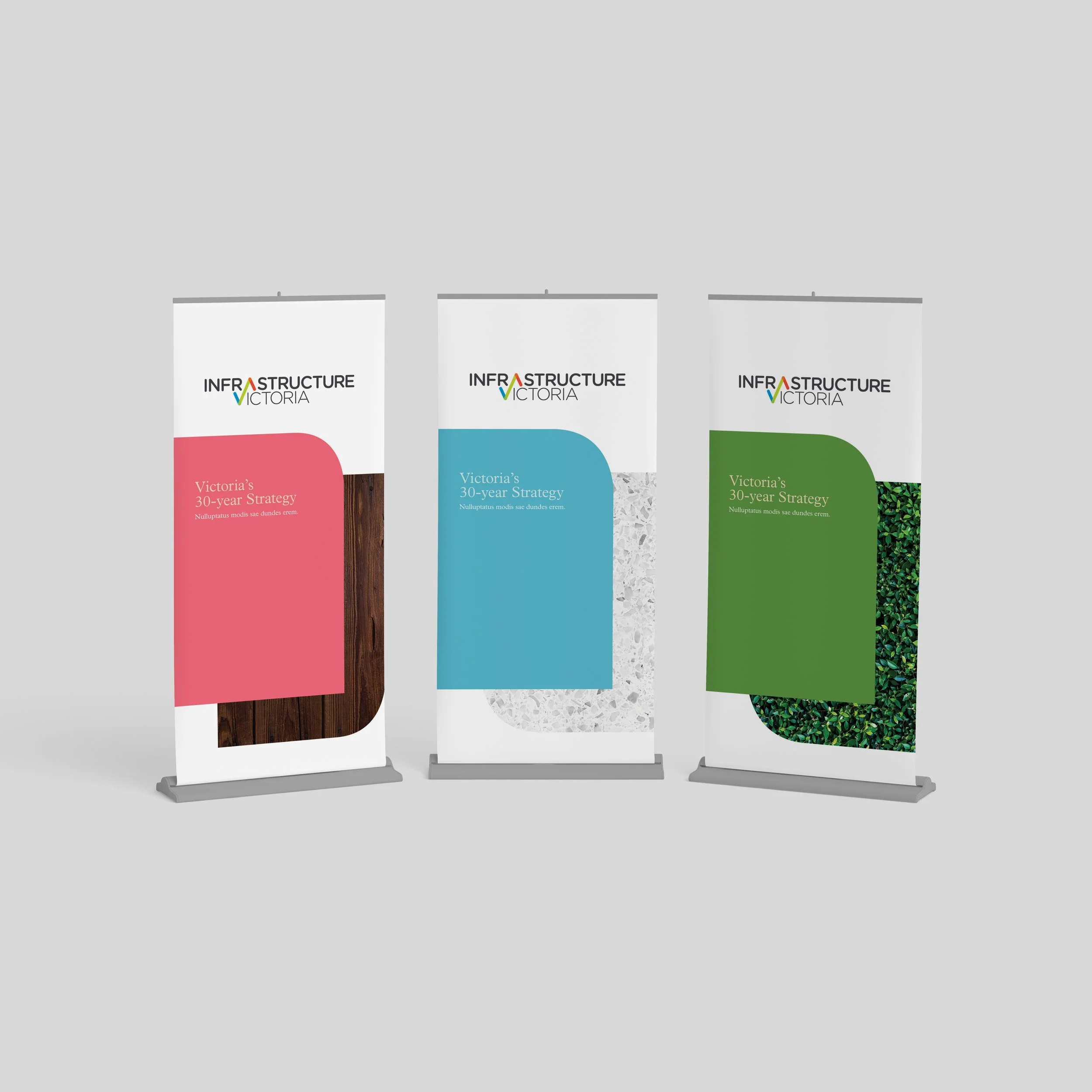 Three retractable banners with the 'Infrastructure Victoria' logo and different color themes: pink, blue, and green, displayed on a gray background.