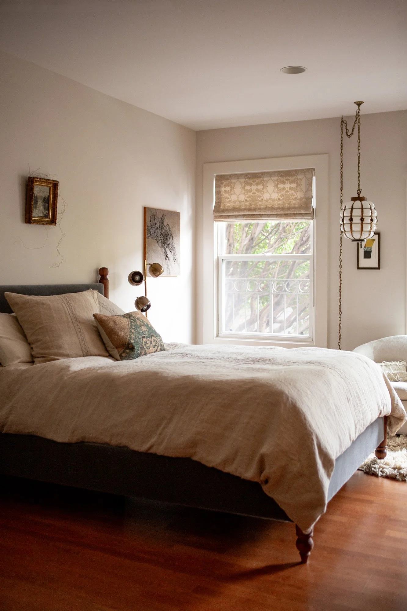 Bedroom at Pine Street Retreat showing a Tempur-Pedic bed with linen bedding, original artwork, brass wall sconce, pendant light, and tree views through a window in a furnished Nob Hill studio