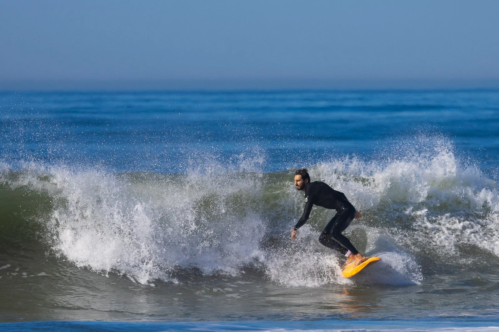 Male surfer in a black wetsuit riding a yellow surfboard on a small wave at the beach.