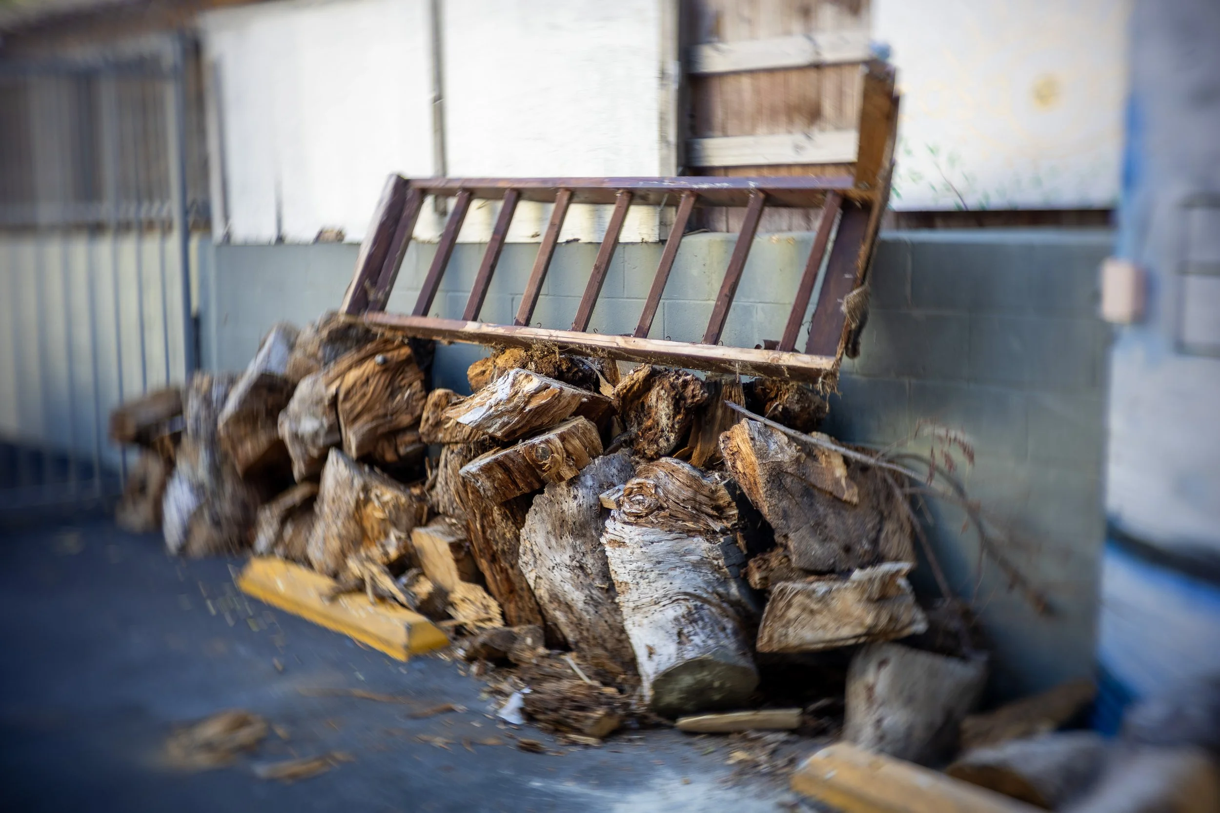 Stack of chopped firewood next to a wooden cart against a gray wall.