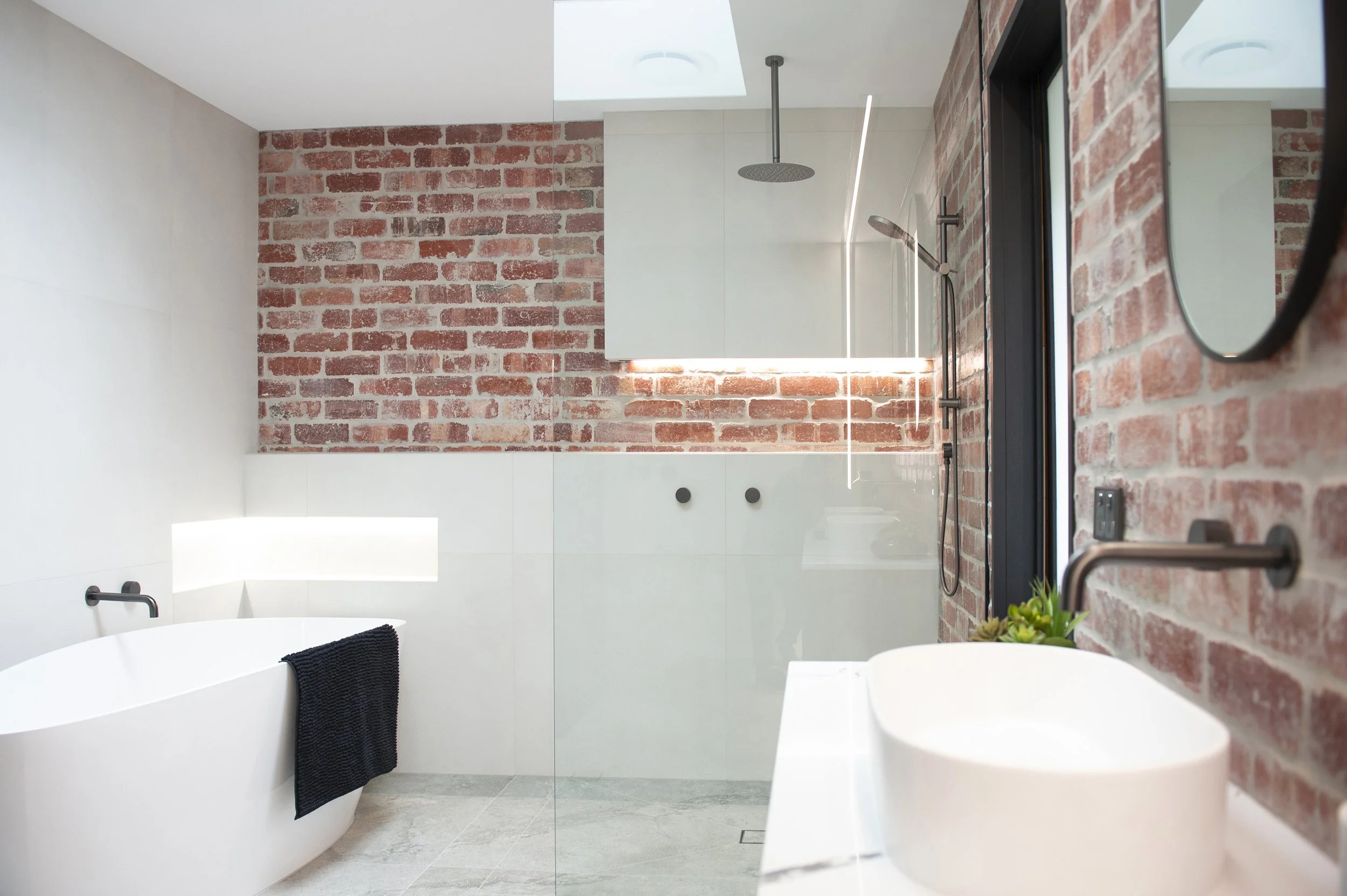 Modern bathroom with white tub, brick wall accents, glass shower, and minimalist fixtures.