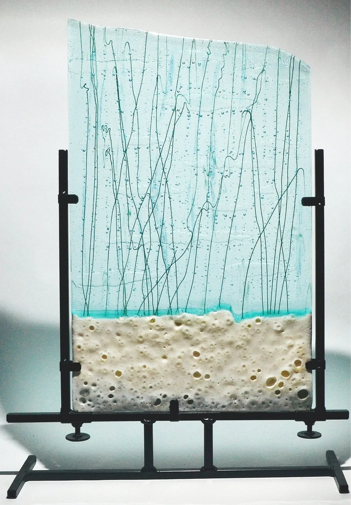A transparent glass panel with water and soap suds at the bottom, mounted on a black metal stand.