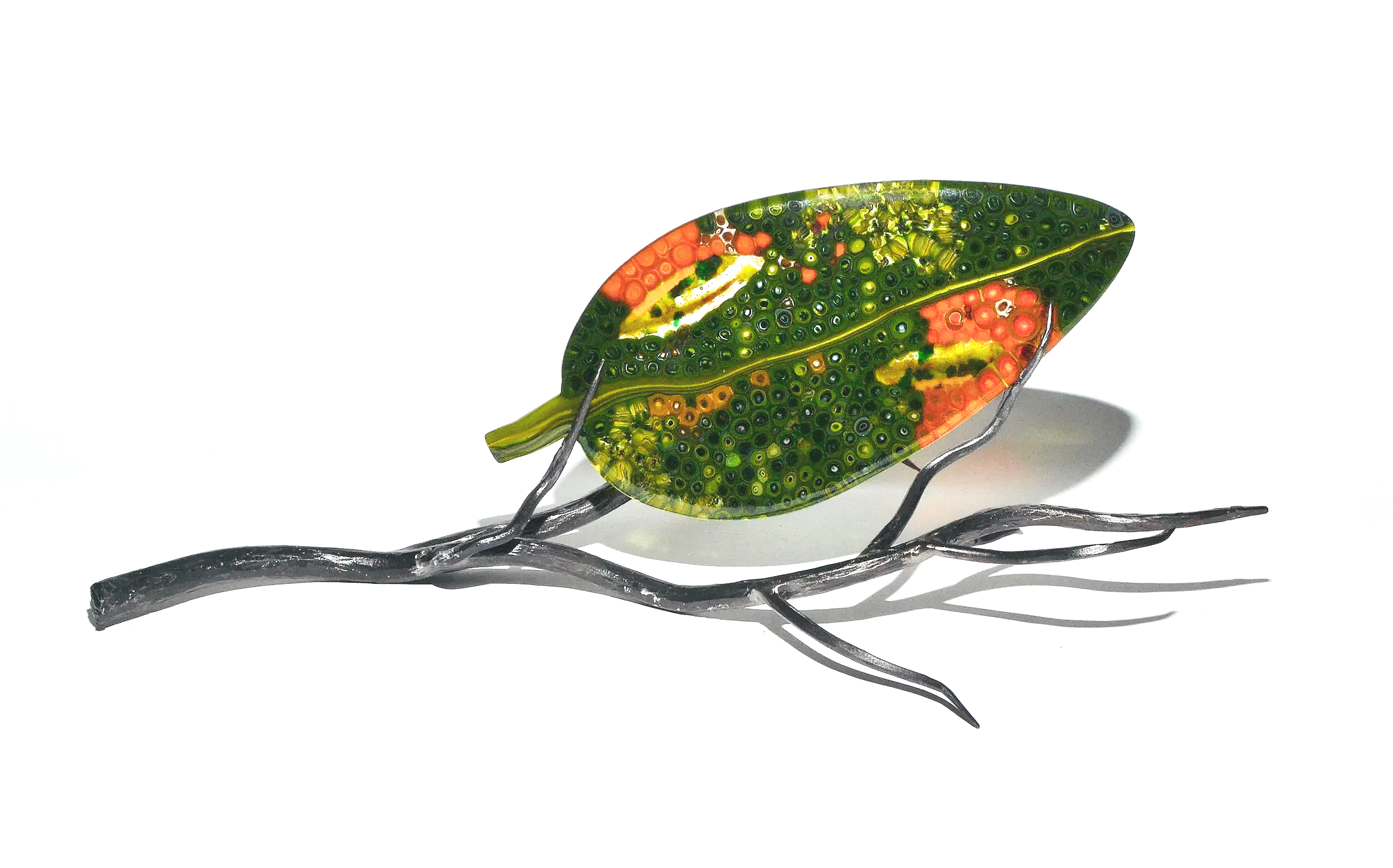 A decorative metal and glass art piece resembling a green leaf with orange and yellow accents, attached to a silver metal branch.