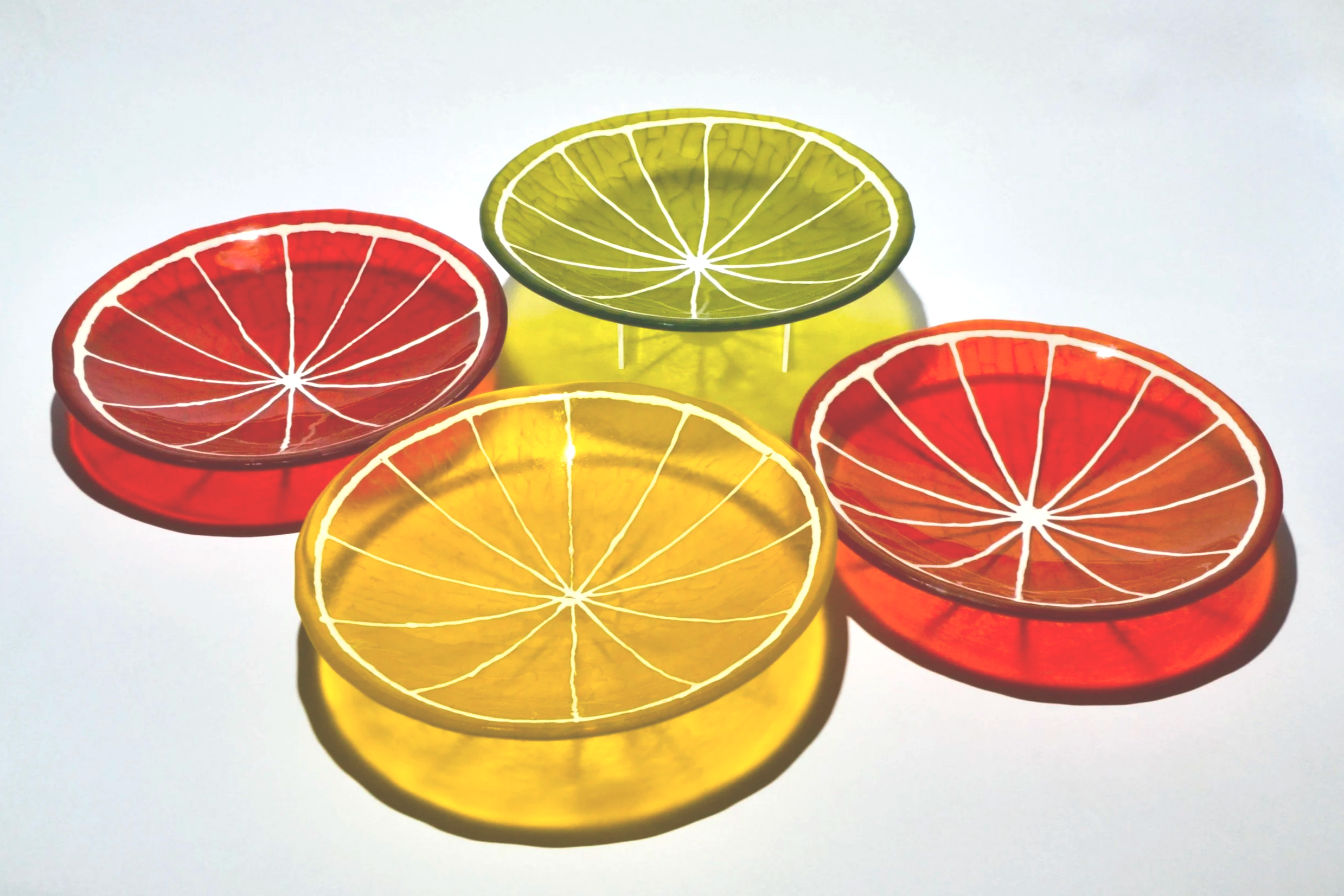 Colorful glass coasters shaped like citrus fruit slices in red, yellow, and green, arranged on a white surface.