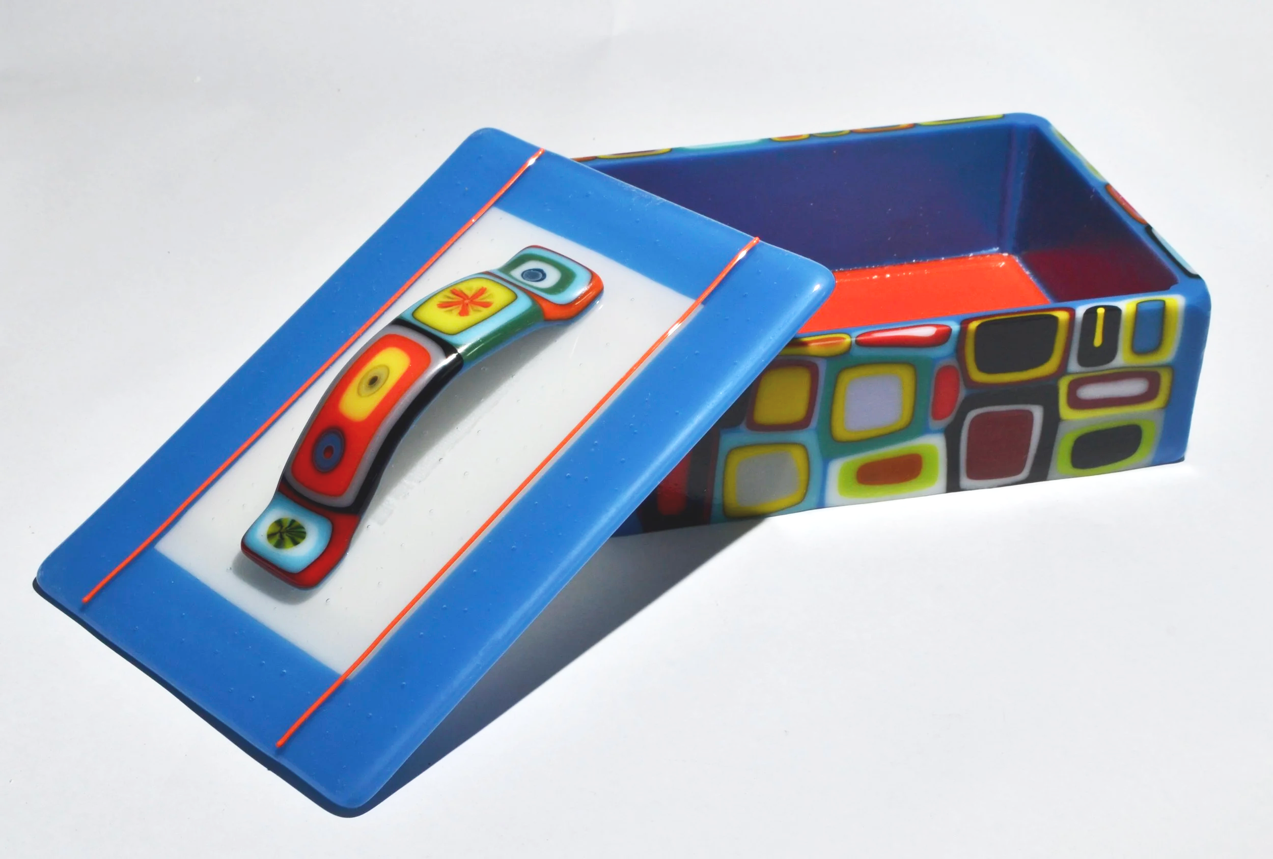 Colorful rectangular decorative box with a lid featuring a curved handle, decorated with abstract patterns in red, yellow, black, white, and green.