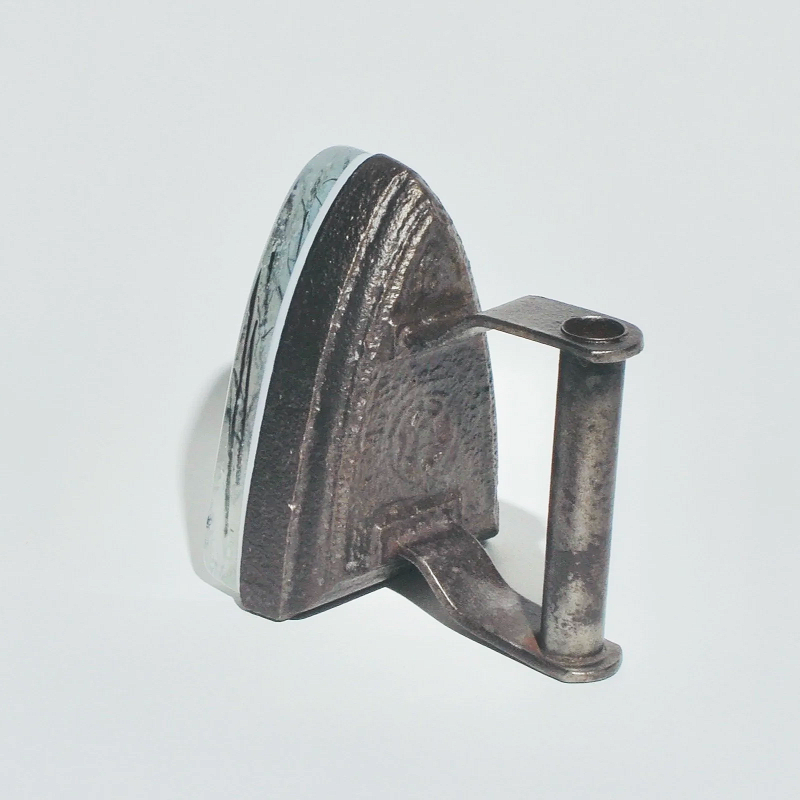 A vintage iron with a round handle and a flat base, standing upright on a white surface.