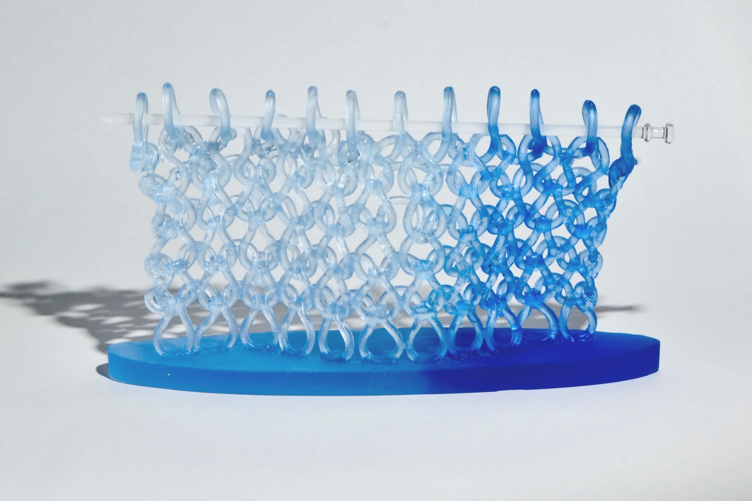 A small loom-made bracelet with a pattern transitioning from light to dark blue, placed on a white surface with shadow.