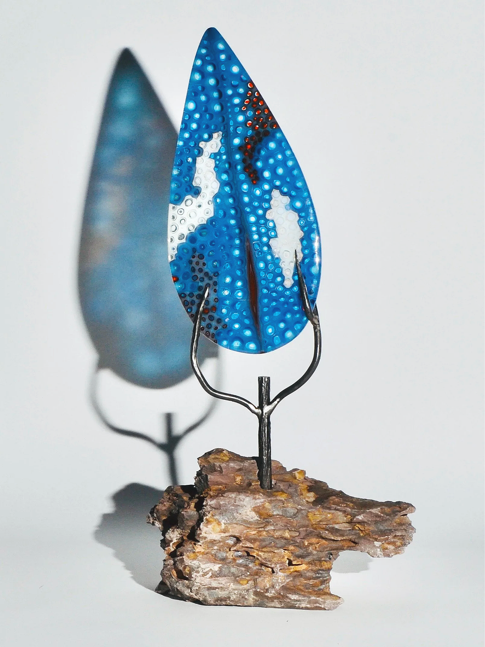 A decorative glass leaf sculpture with a blue, white, and black pattern, mounted on a wooden base.