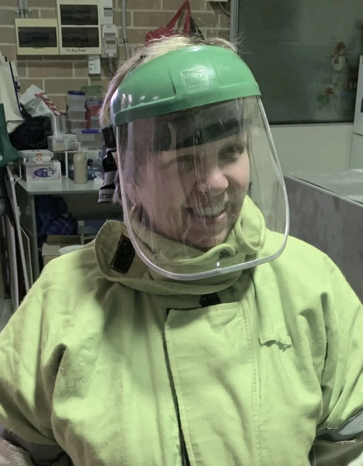 A person wearing a face shield and yellow protective gear in a medical or industrial setting.