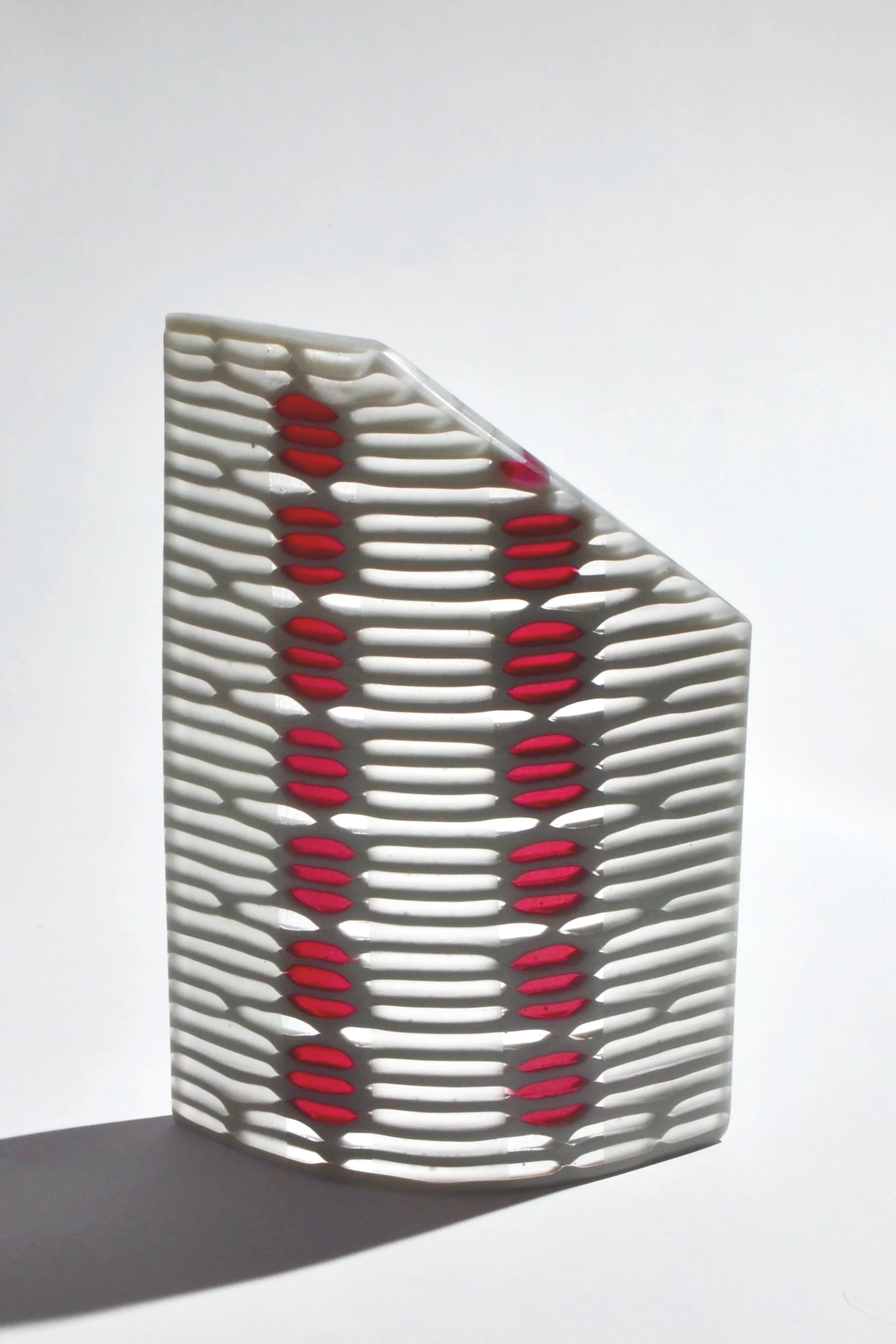 A white chair with horizontal slats and red cushioned oval-shaped seats, casting a shadow on a white surface.