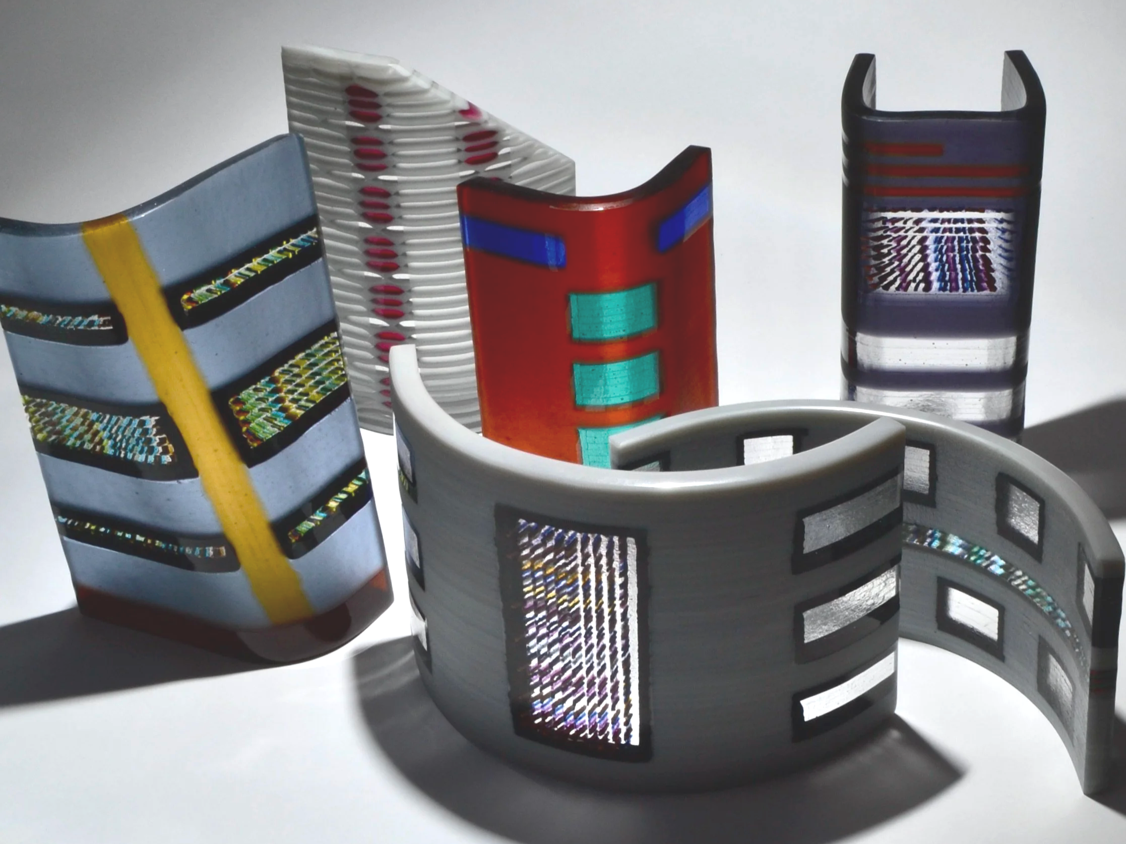 Multiple colorful 3D-printed bracelets with various geometric and pattern designs, placed on a white surface.
