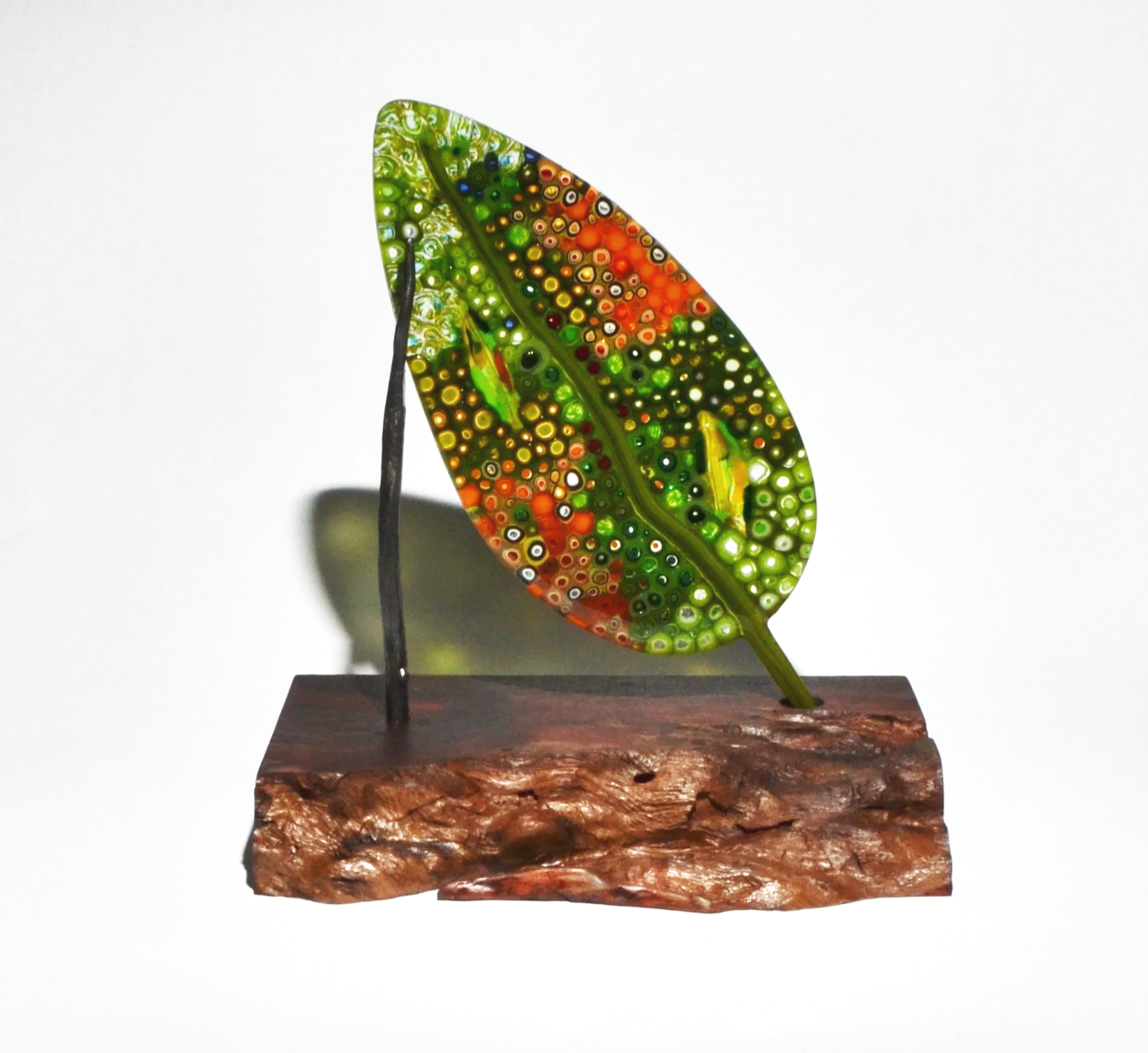 A decorative glass leaf with colorful concentric circles, mounted on a wooden base with a metal support.