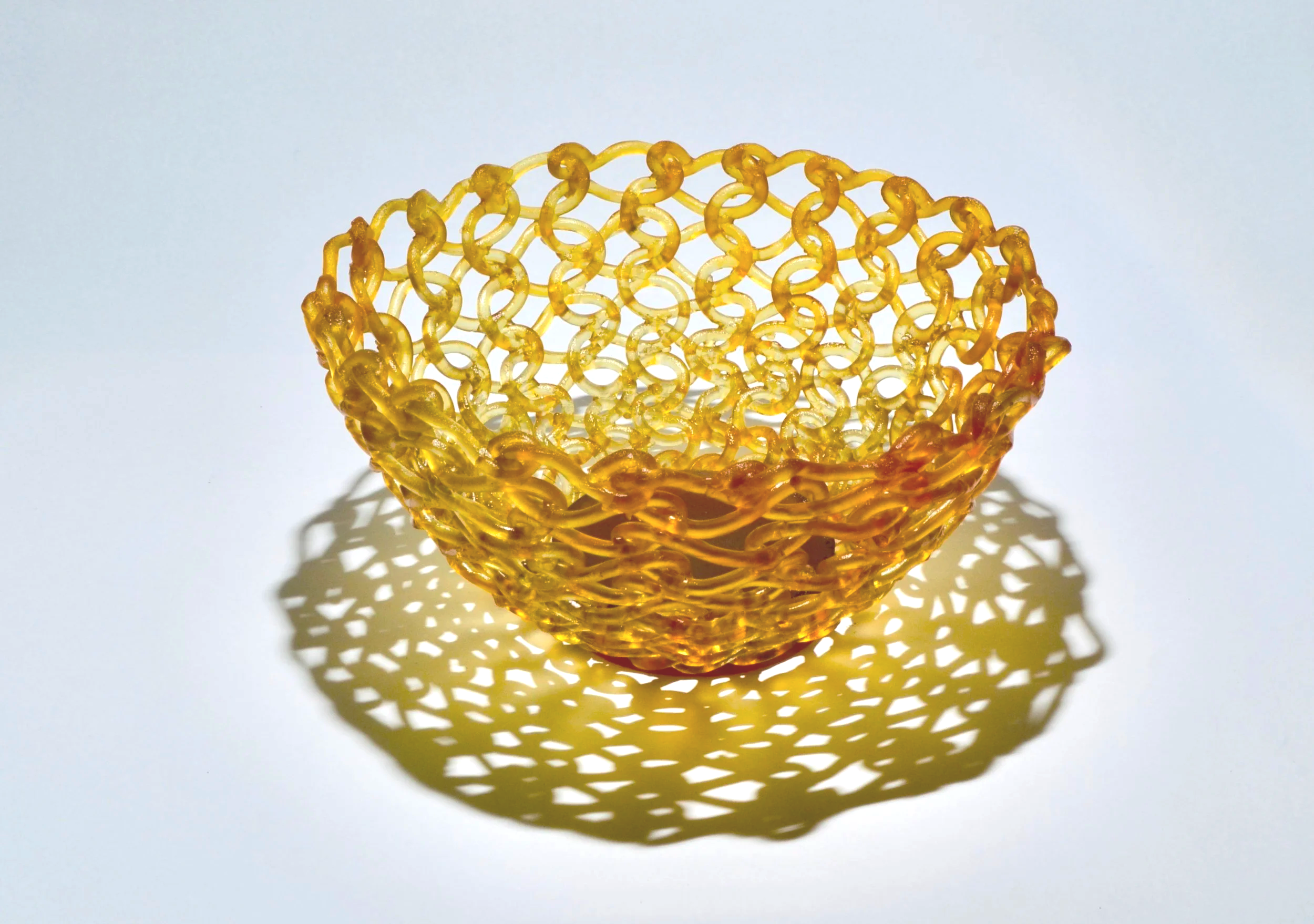 Yellow plastic open-weave basket casting a shadow on a white surface.