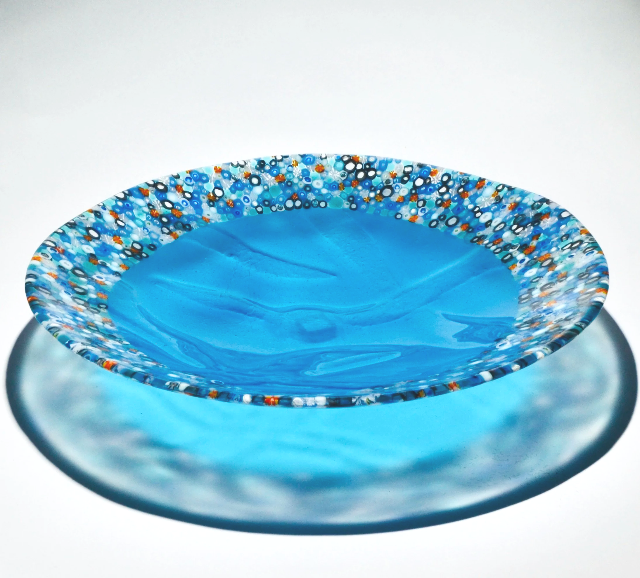 Colorful glass bowl with a blue interior and multicolored speckles along the rim, placed on a reflective surface.