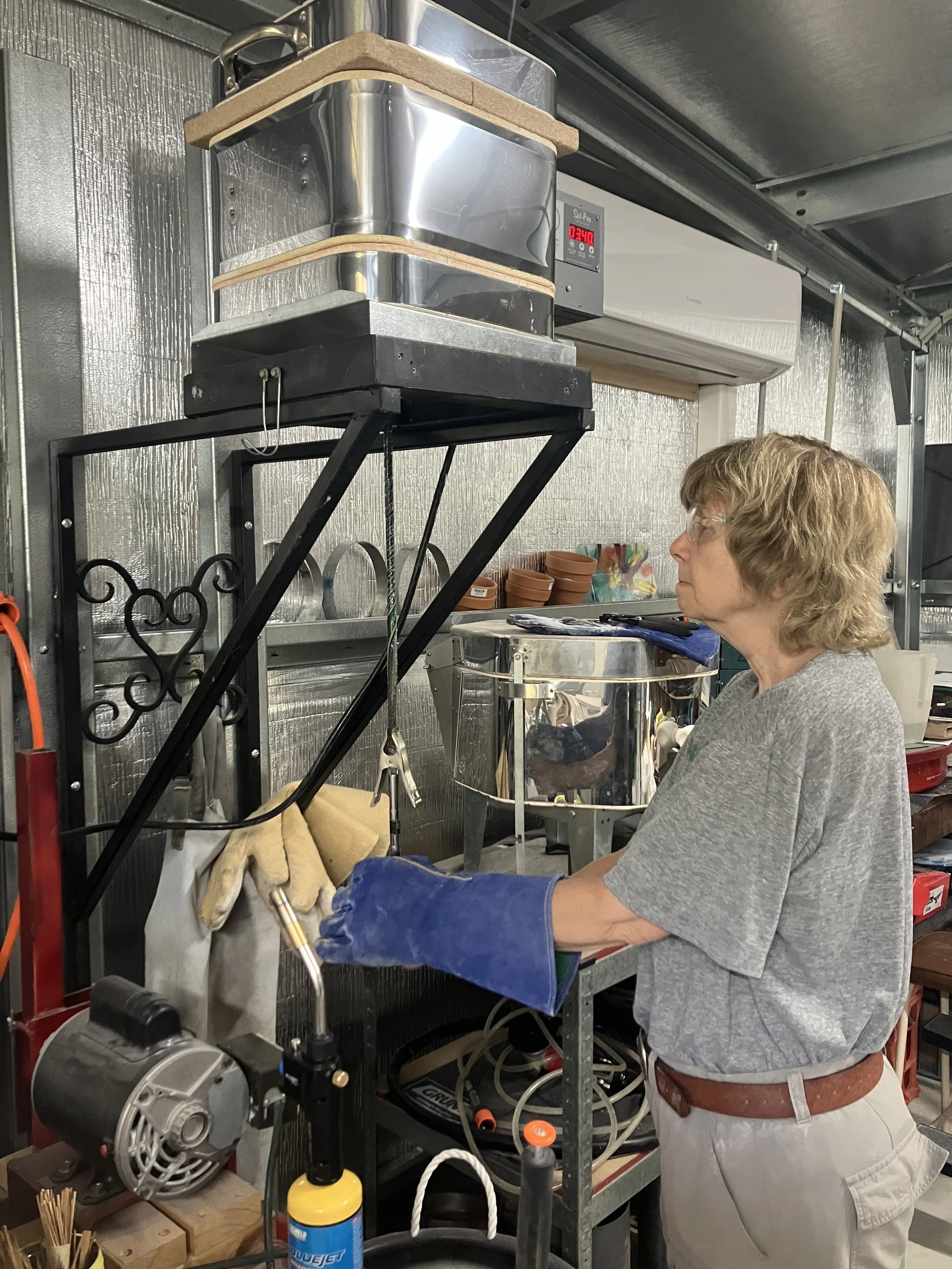 A woman wearing safety glasses and gloves working with equipment in a workshop or lab environment.