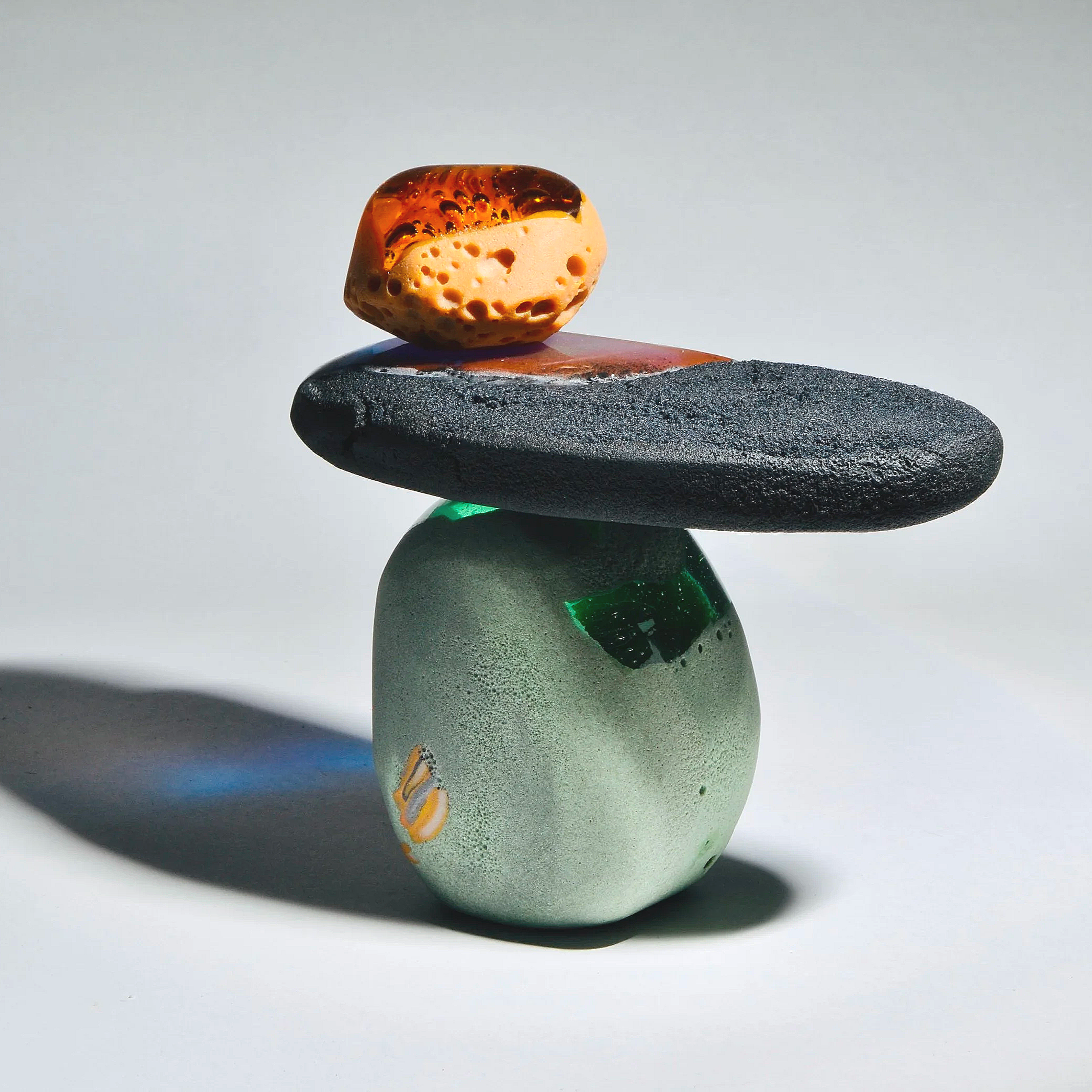A stacked arrangement of four stones of varying colors and textures, with a small orange porous stone on top.