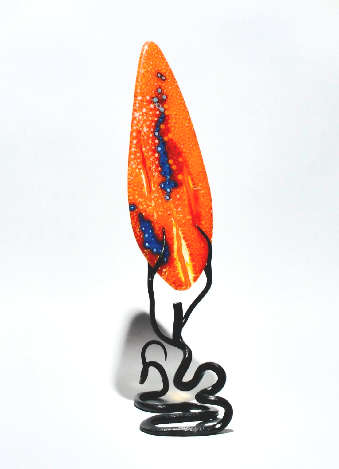 An artistic glass sculpture of an orange and red leaf with blue accents, mounted on black twisted metal stands.