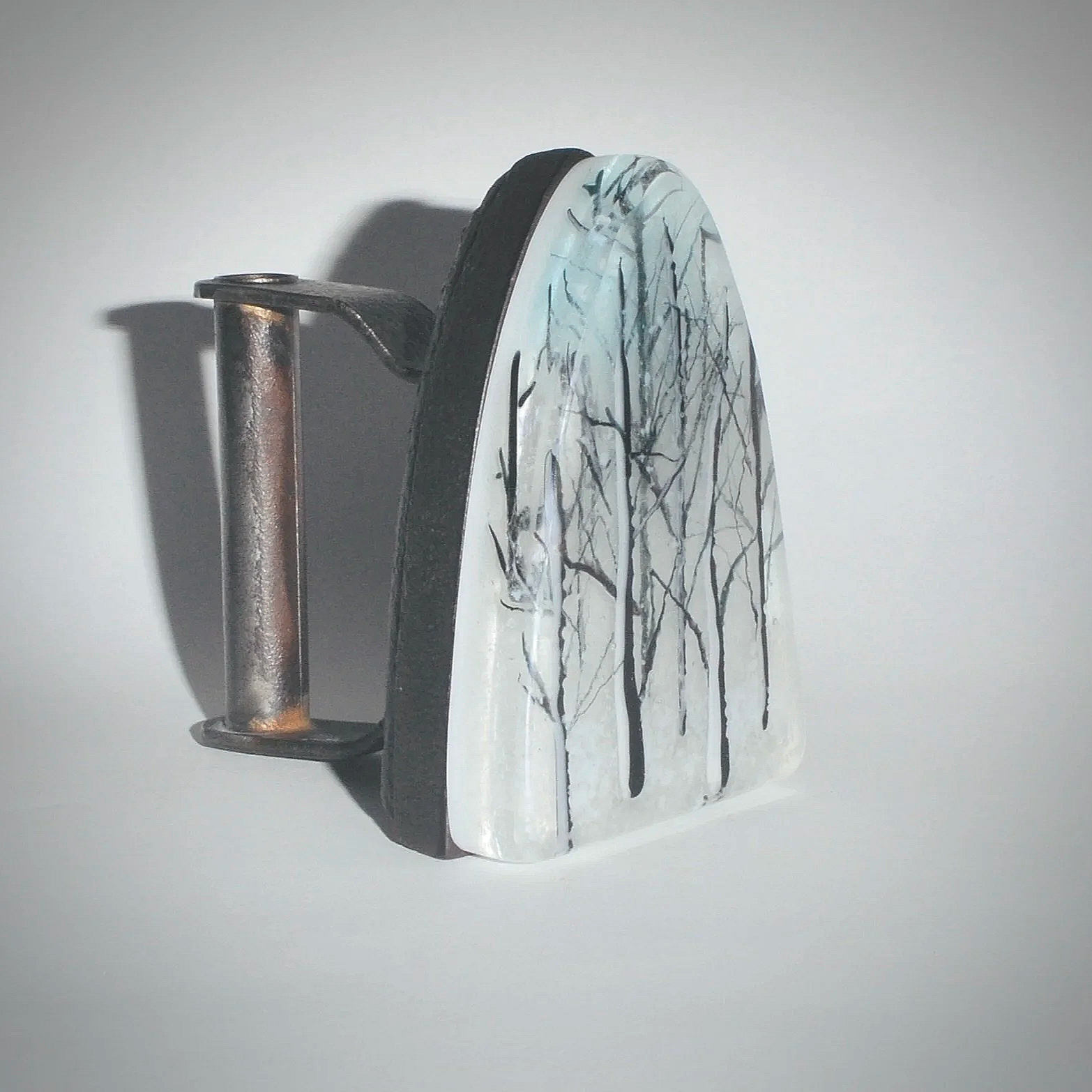 An iron with a painted design of bare tree branches on its surface, placed against a plain white background.