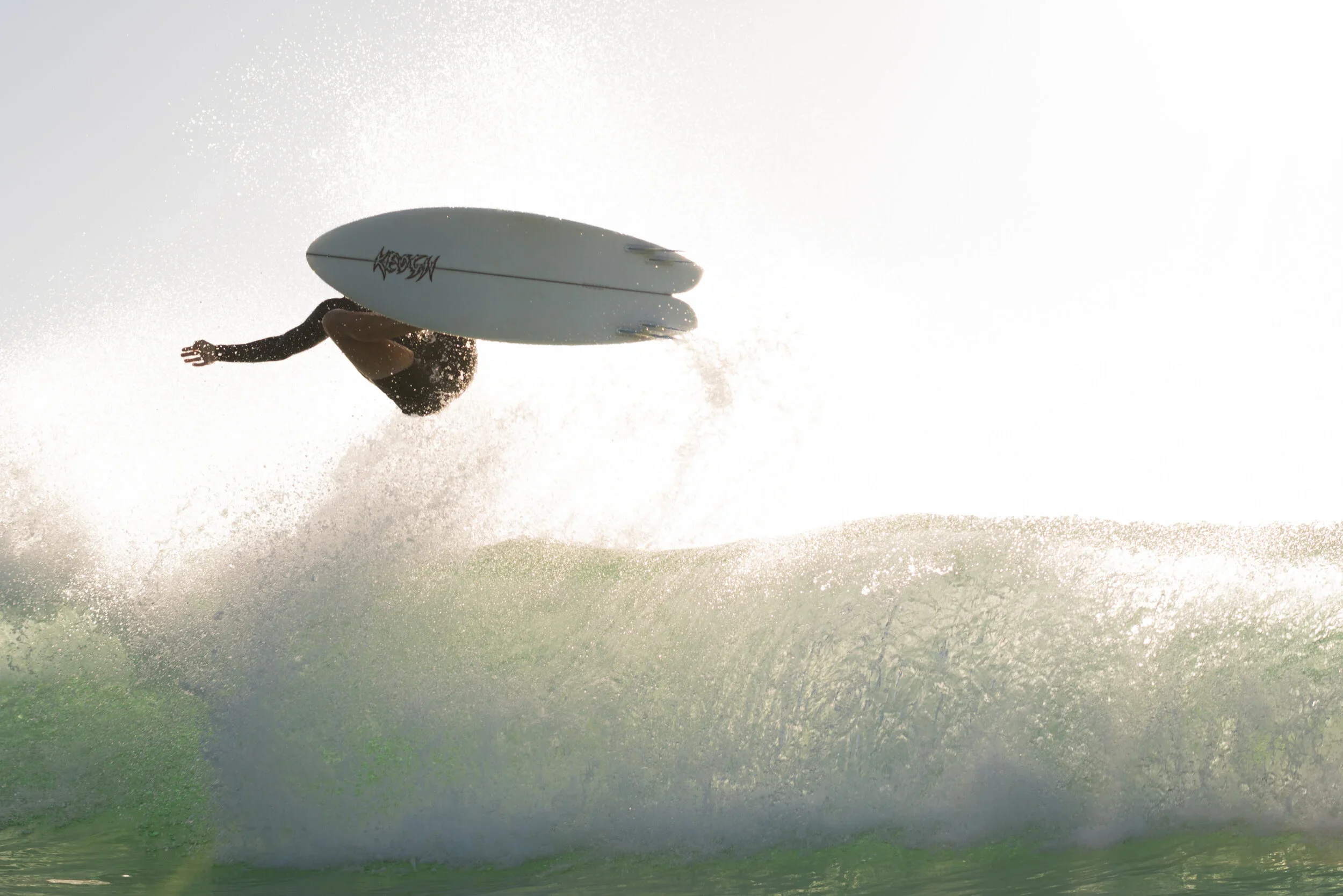 A surfer performing an aerial trick on a surfboard above the wave at sunset or sunrise.