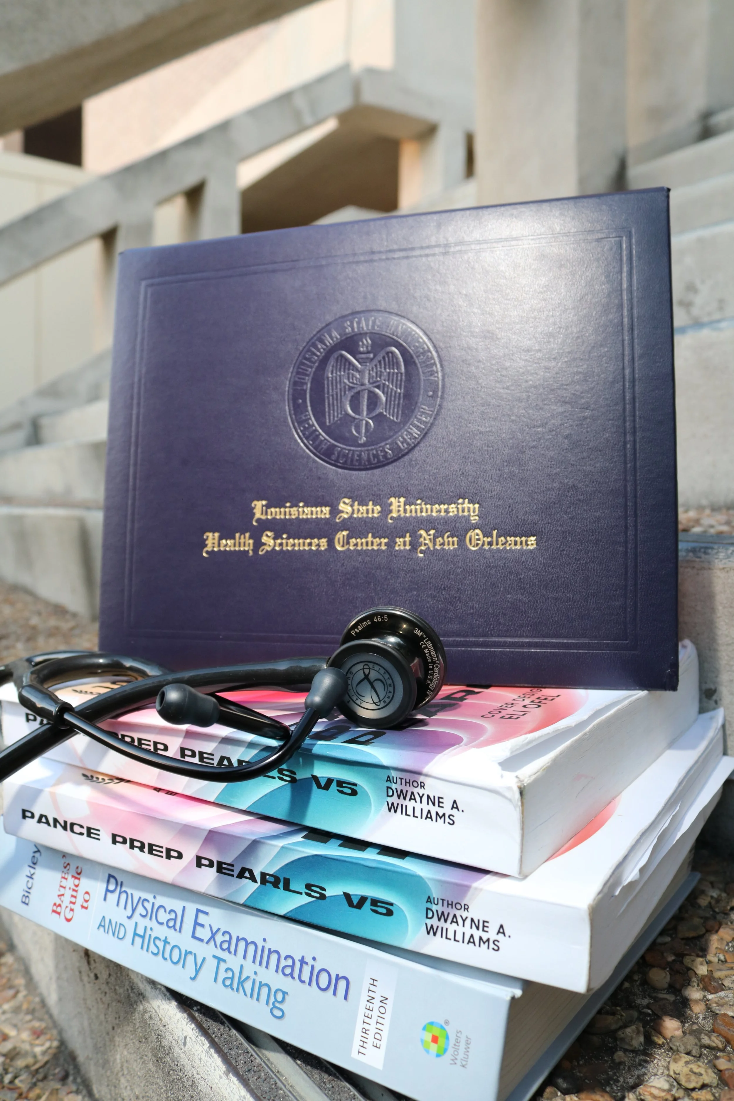 A stack of educational books about physical examination and history taking, with a pair of black and gray earbuds resting on the top book, which is titled 'Pearls V5'. The topmost book in the stack has a dark blue cover with gold lettering and the lo