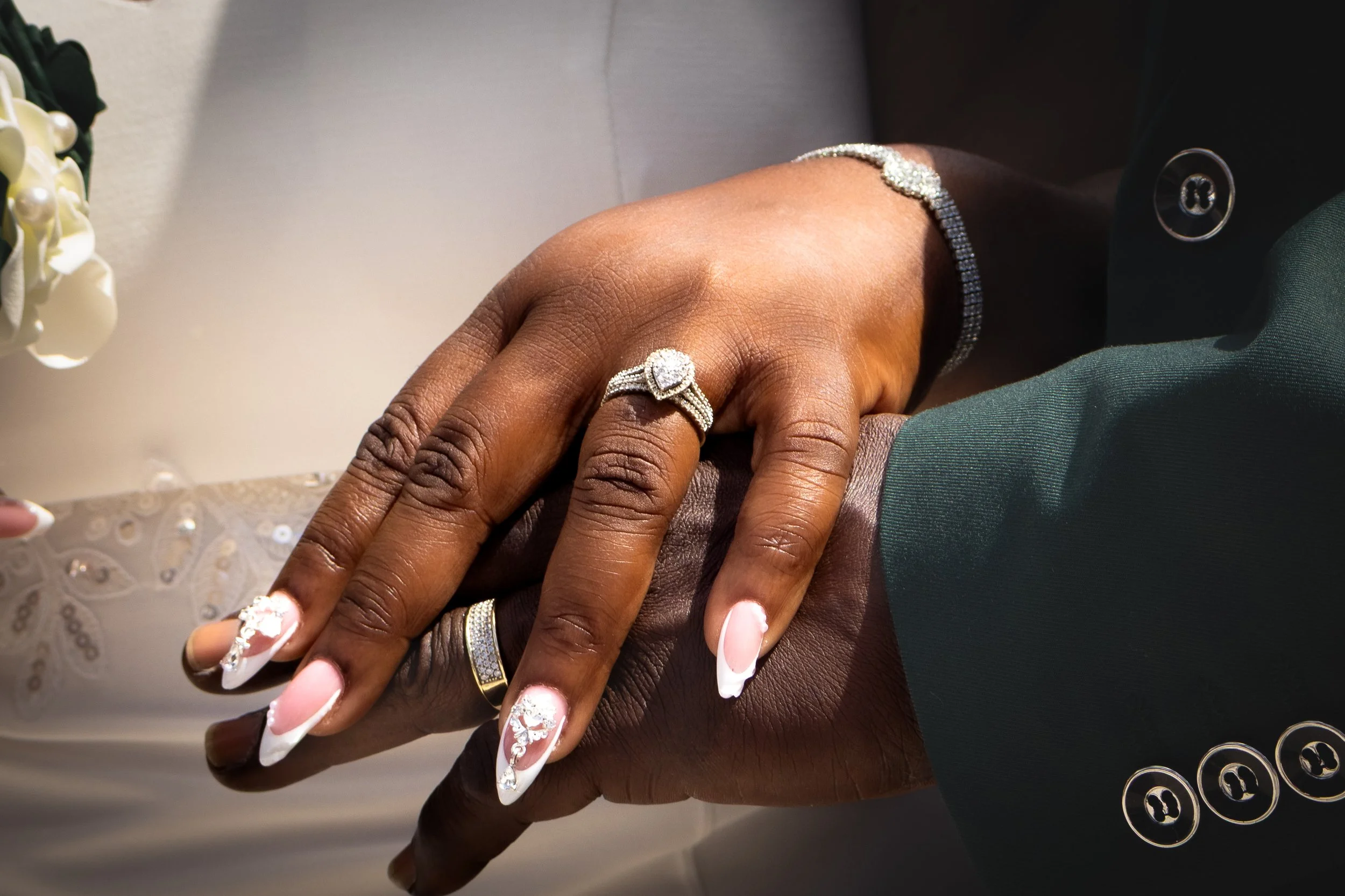 Close-up of two hands intertwined, showing wedding rings and elegant nail art with white tips and silver embellishments.