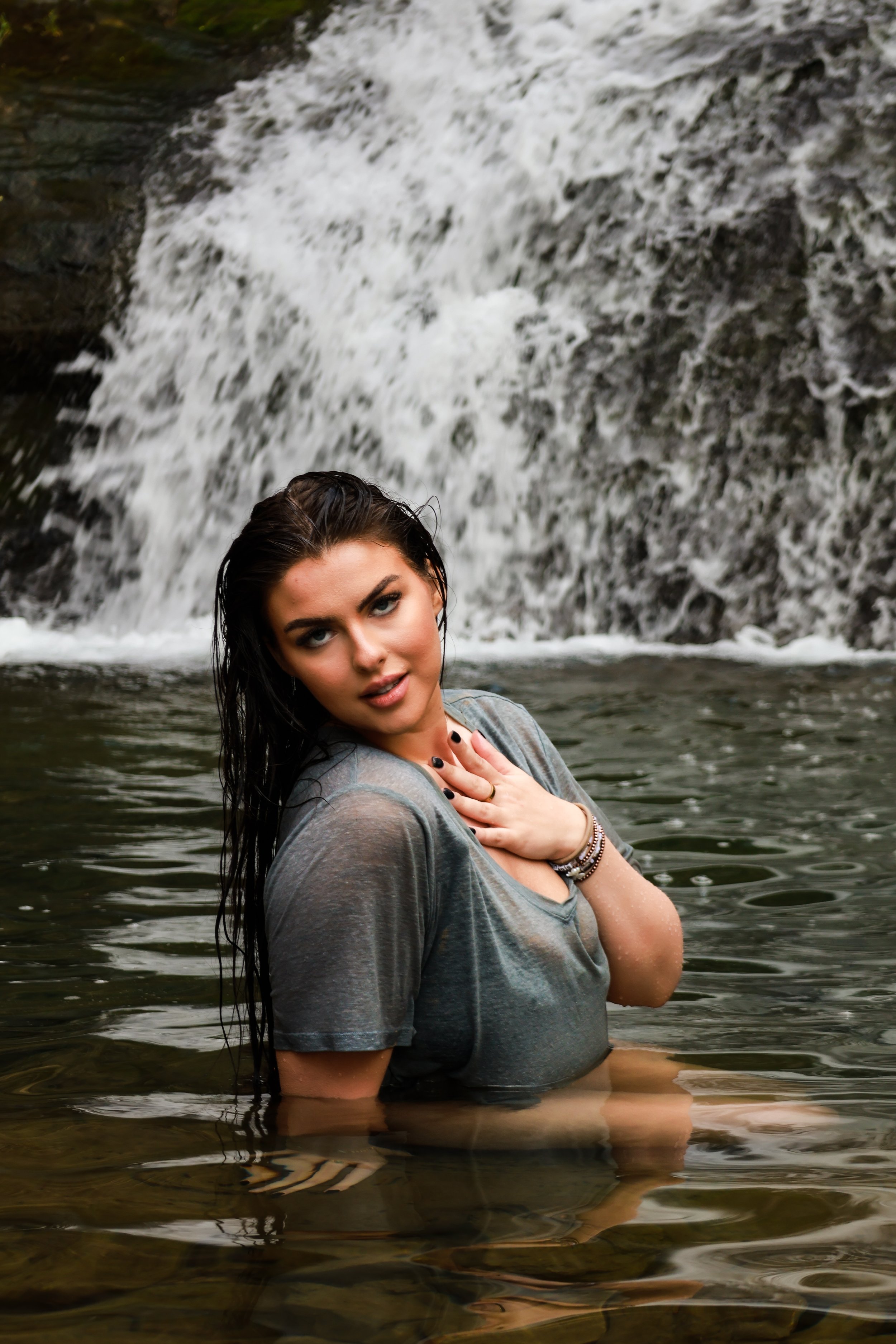 Woman standing in water with waterfall in the background.
