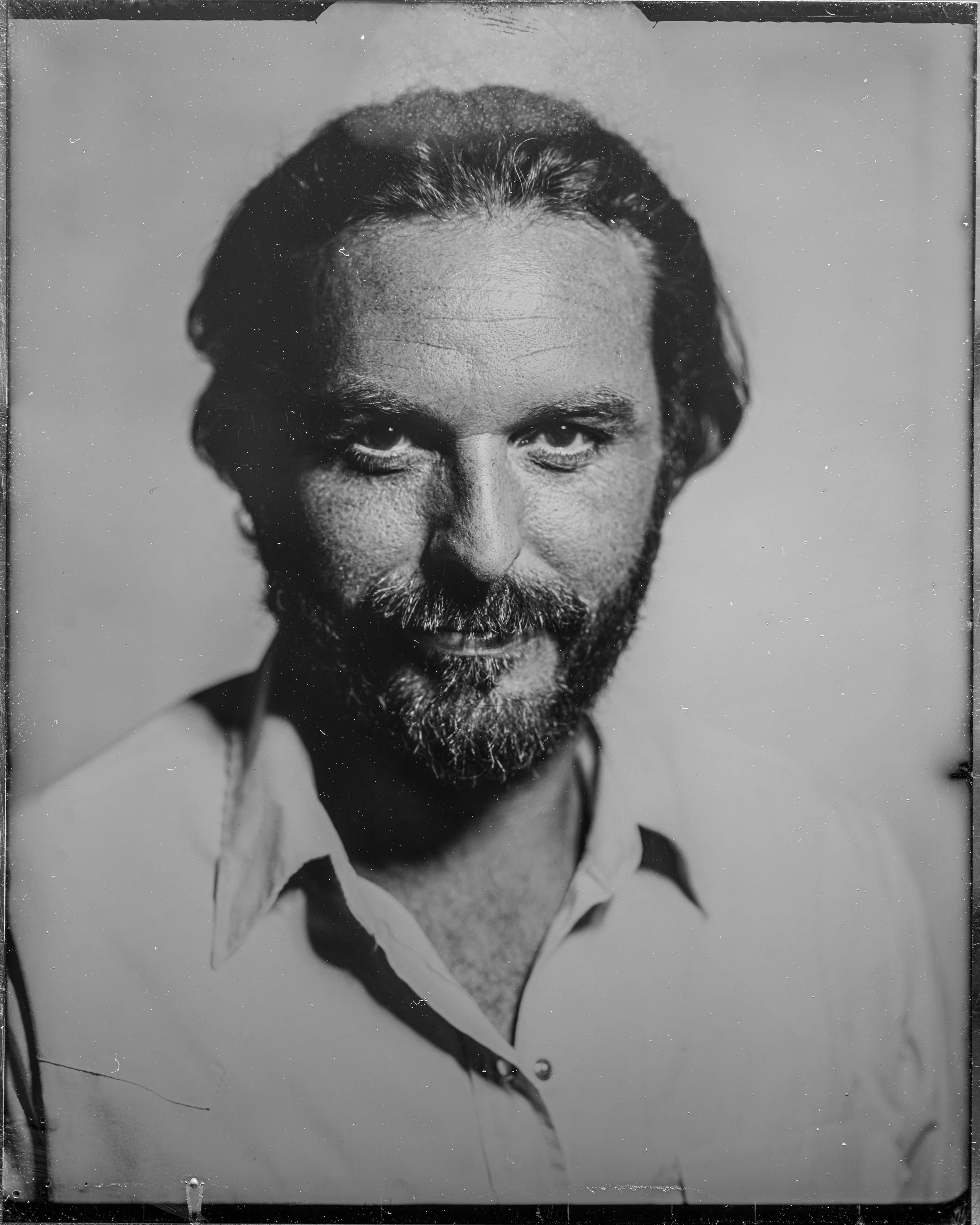 Black and white photograph of a man with a beard and mustache, wearing a collared shirt, looking into the camera with a serious expression.