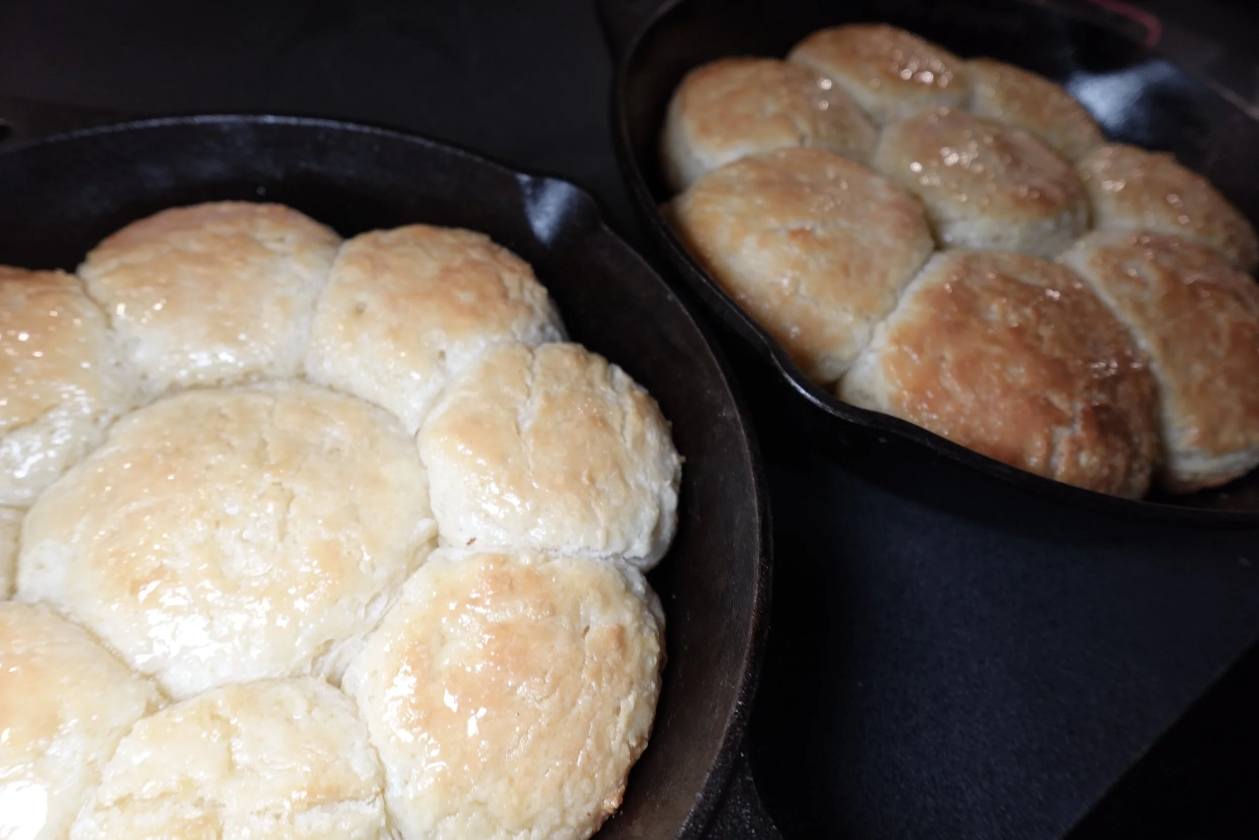 Cast iron skillets with freshly baked biscuits, some topped with butter.