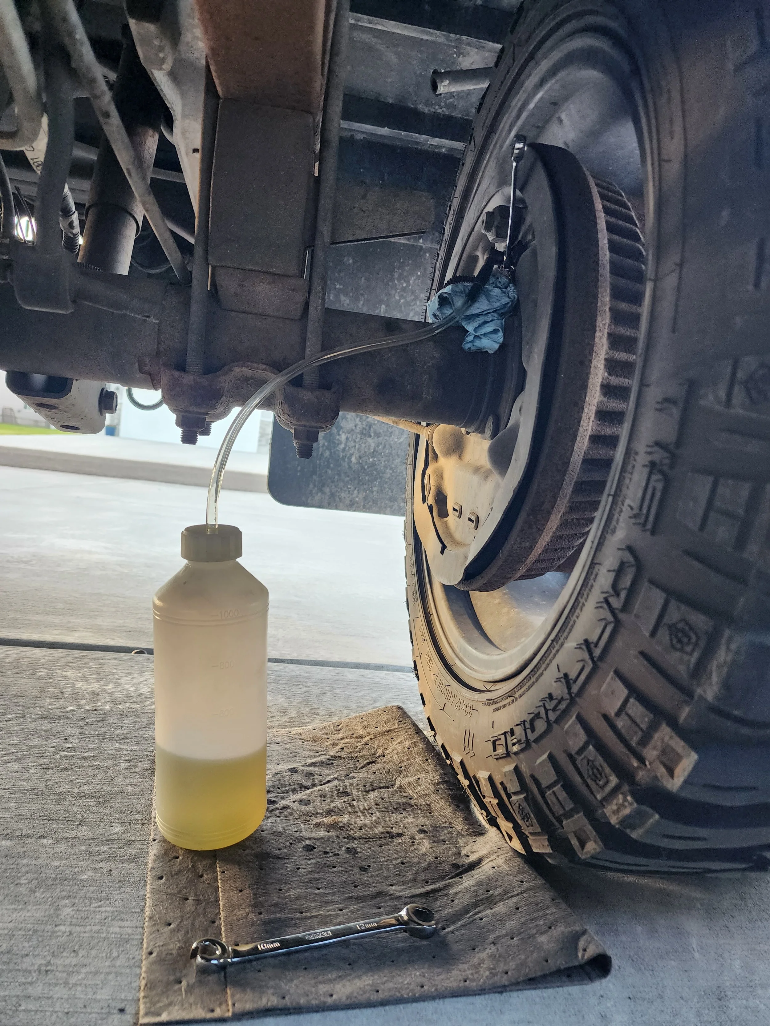 A vehicle getting a brake fluid flush service and a bottle of yellow-green brake fluid and a wrench nearby.