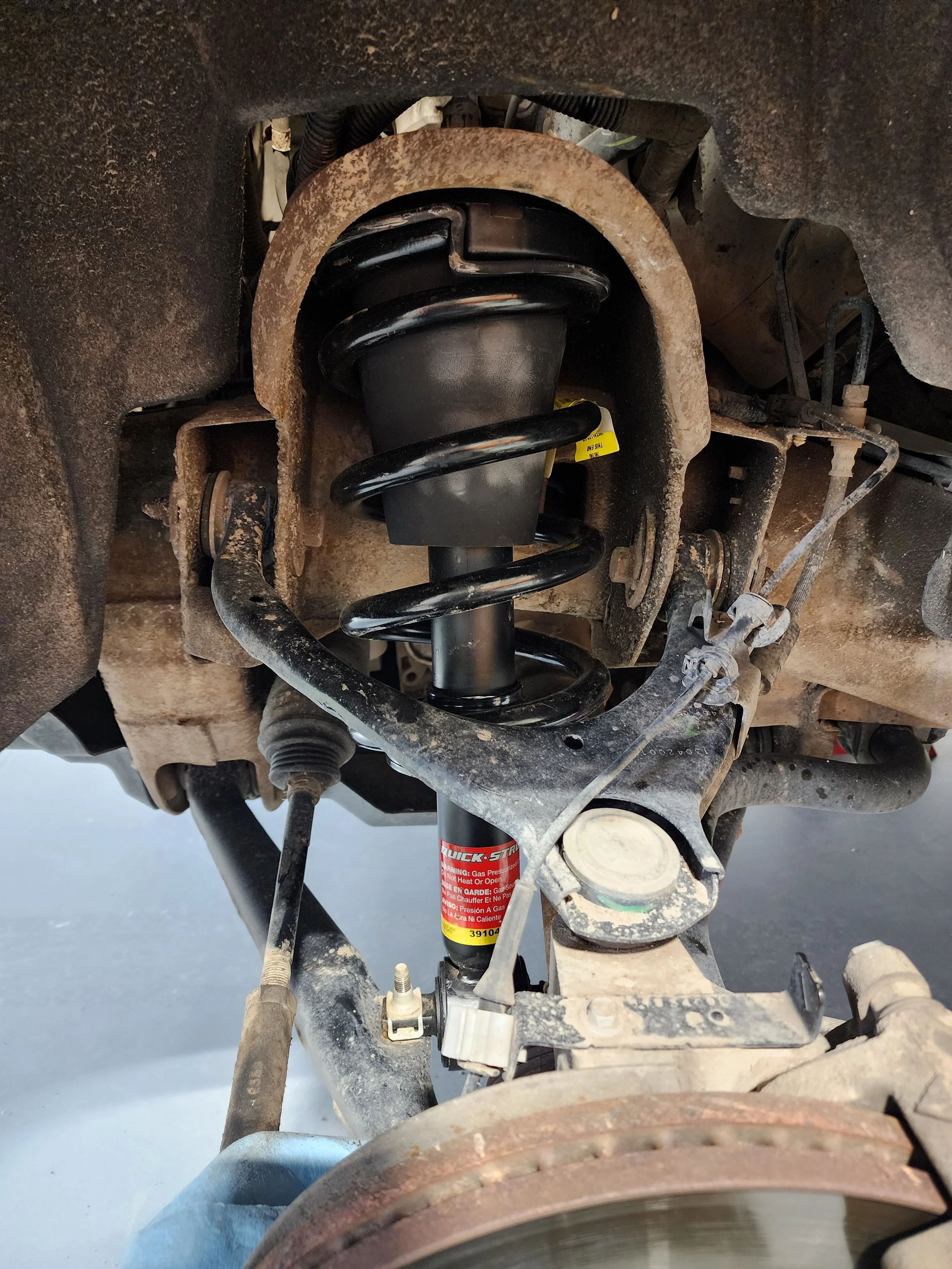 View of a vehicle's suspension system showing a coil spring, shock absorber, brake rotor, and various suspension components.