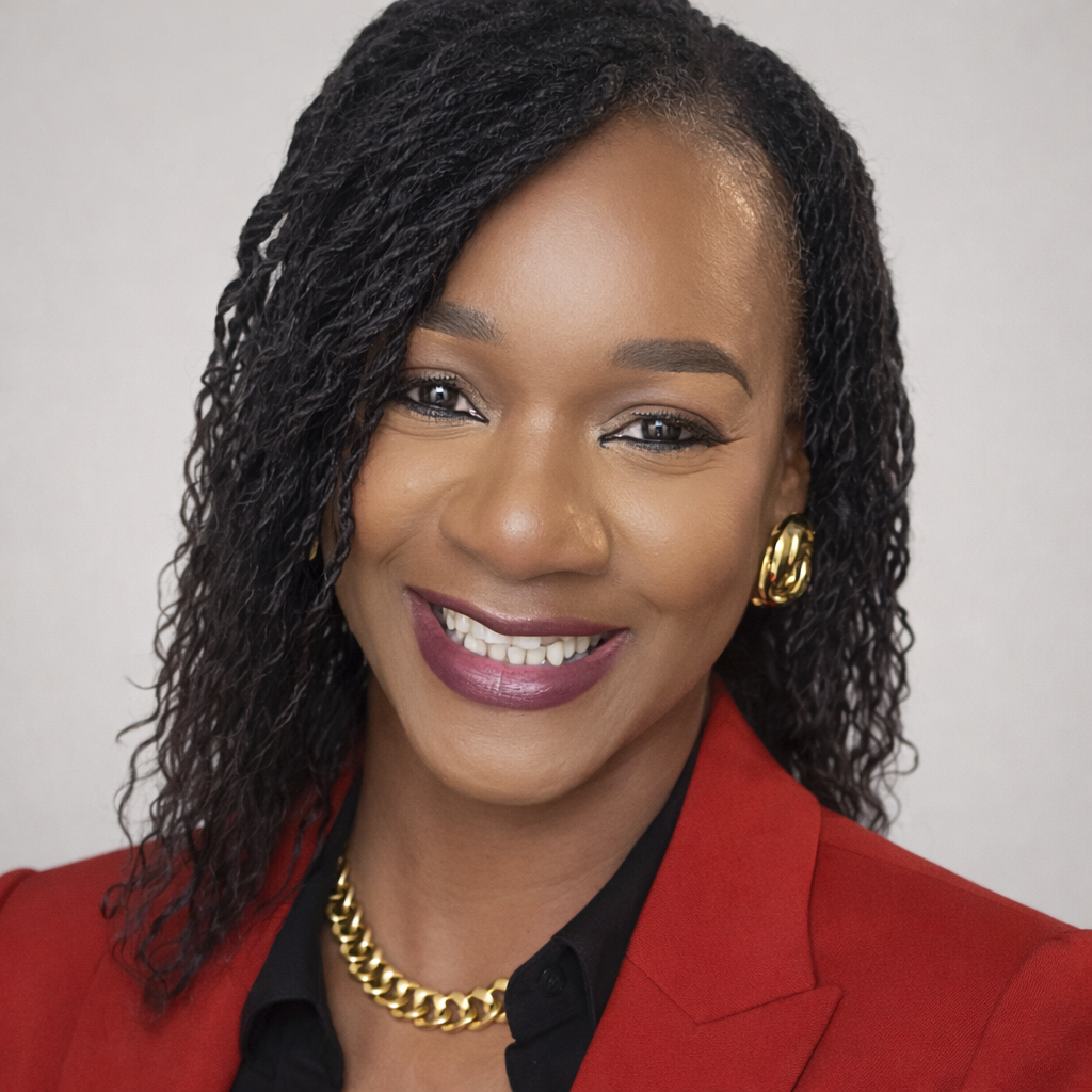 Portrait of a smiling woman with curly black hair wearing a red blazer, black blouse, gold earrings, and a gold chain necklace.