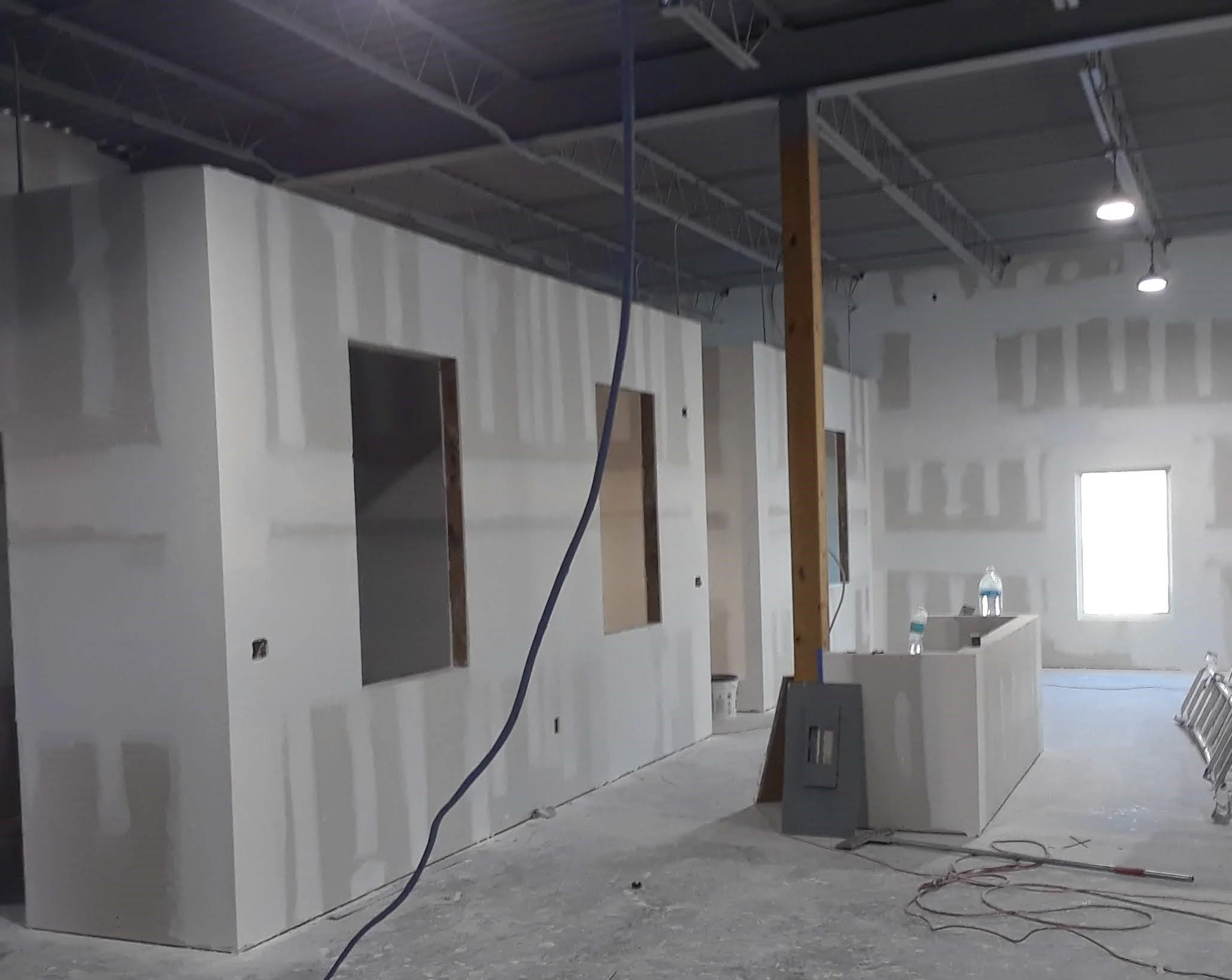 Building interior under construction with drywall installation and unfinished walls, visible electrical wiring, and construction materials on the floor.