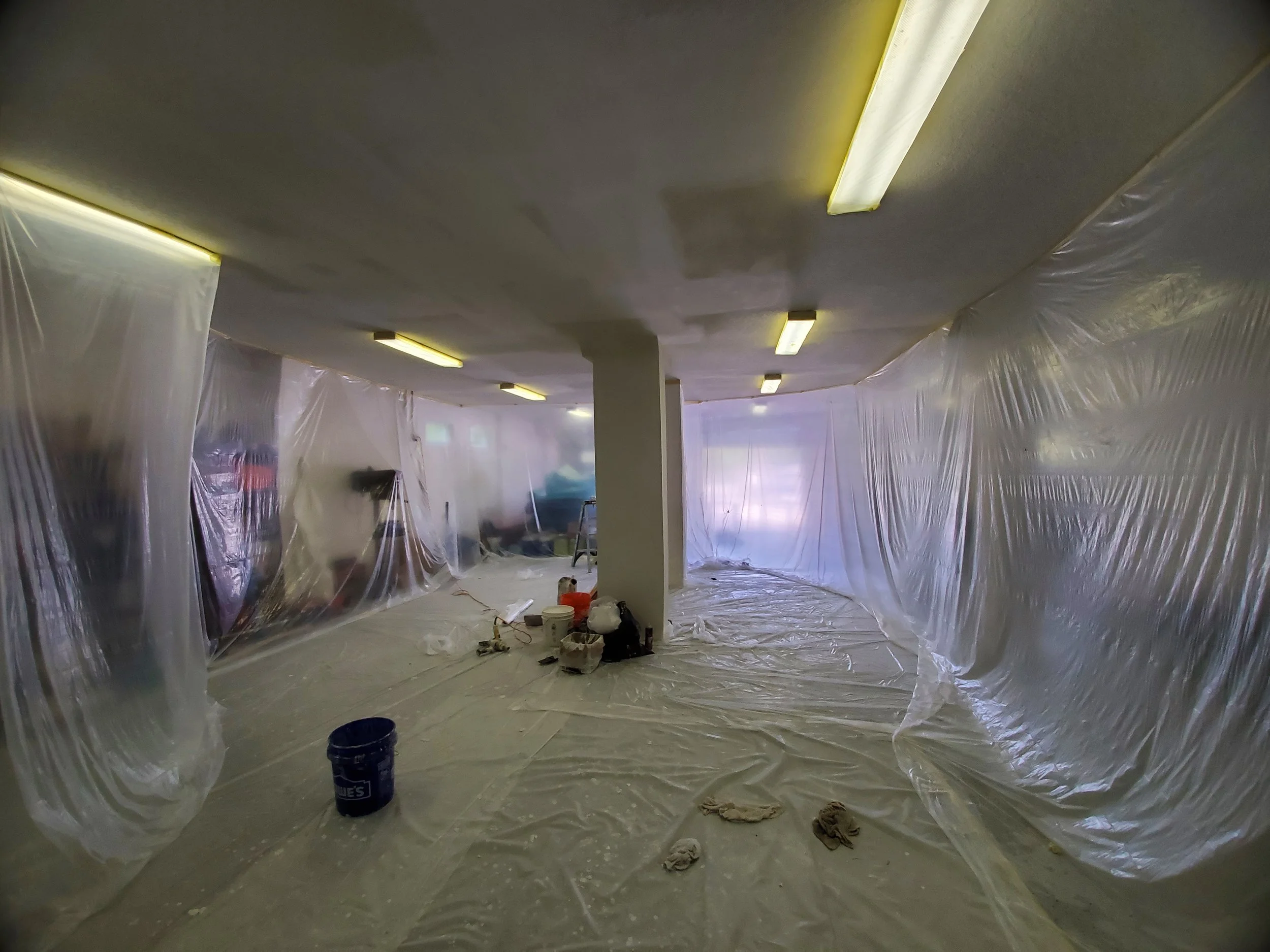 Garage ceiling project sealed with plastic sheeting covering the walls and floor, with drywall tools and materials on the job site to repair loose tape and cracked seams.