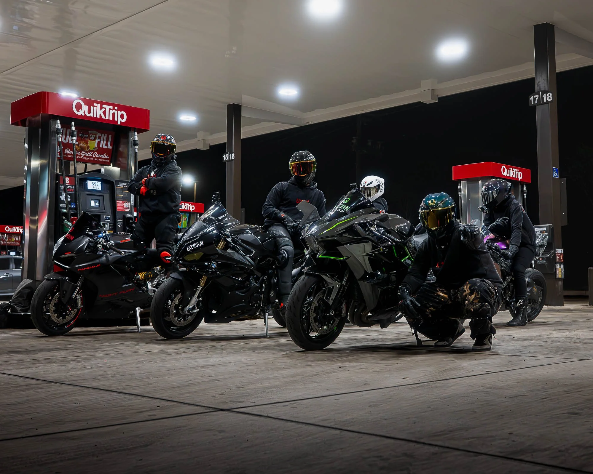 EXCIDIVM riders with sport motorcycles wearing black streetwear at gas station night