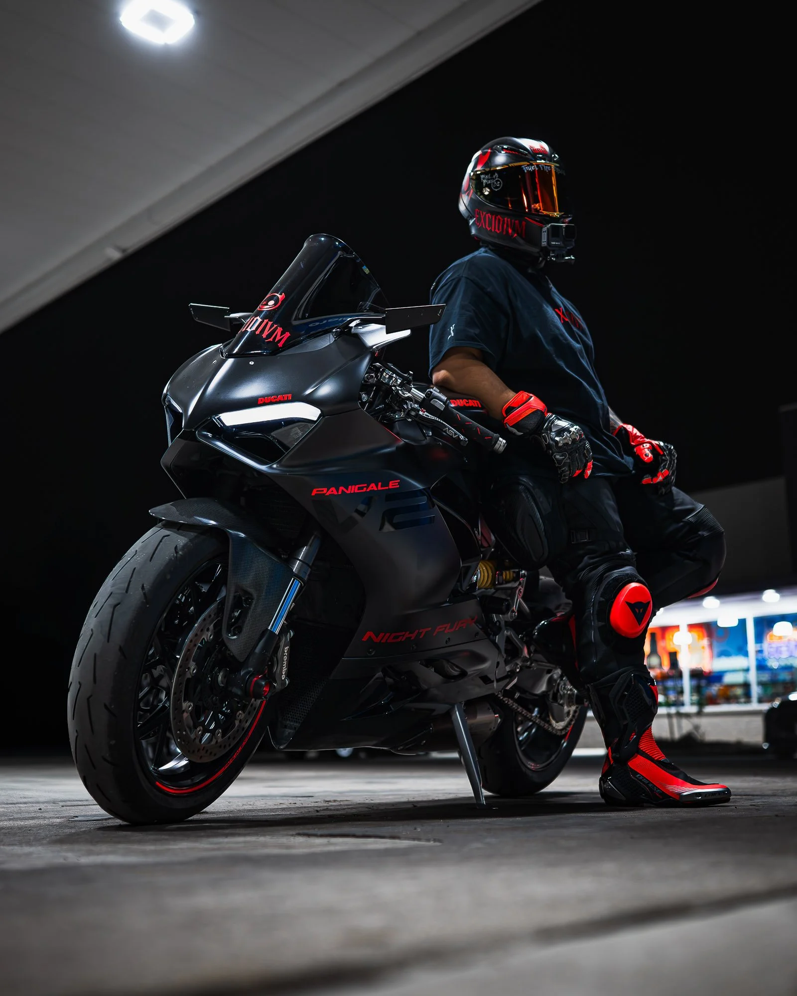 EXCIDIVM rider sitting on Ducati Panigale sport motorcycle wearing black streetwear at night