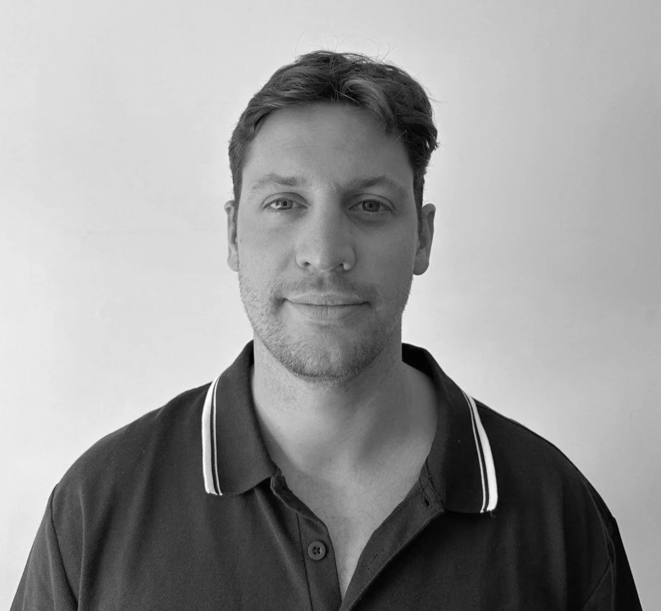 A black and white portrait of a man wearing a dark polo shirt with a light background.