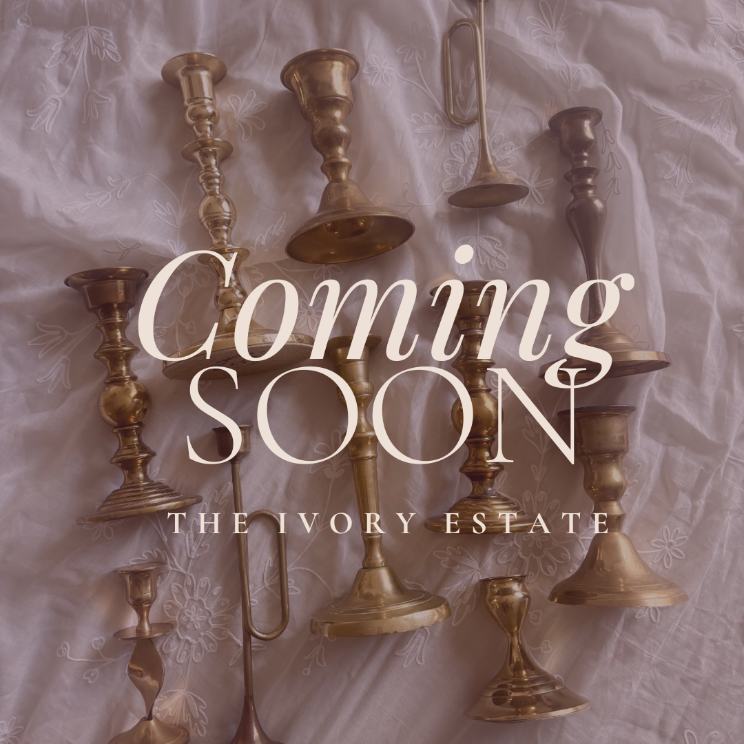 Multiple brass candlesticks on a embroidered white fabric, with the text 'Coming Soon' and 'The Ivory Estate' overlaid.