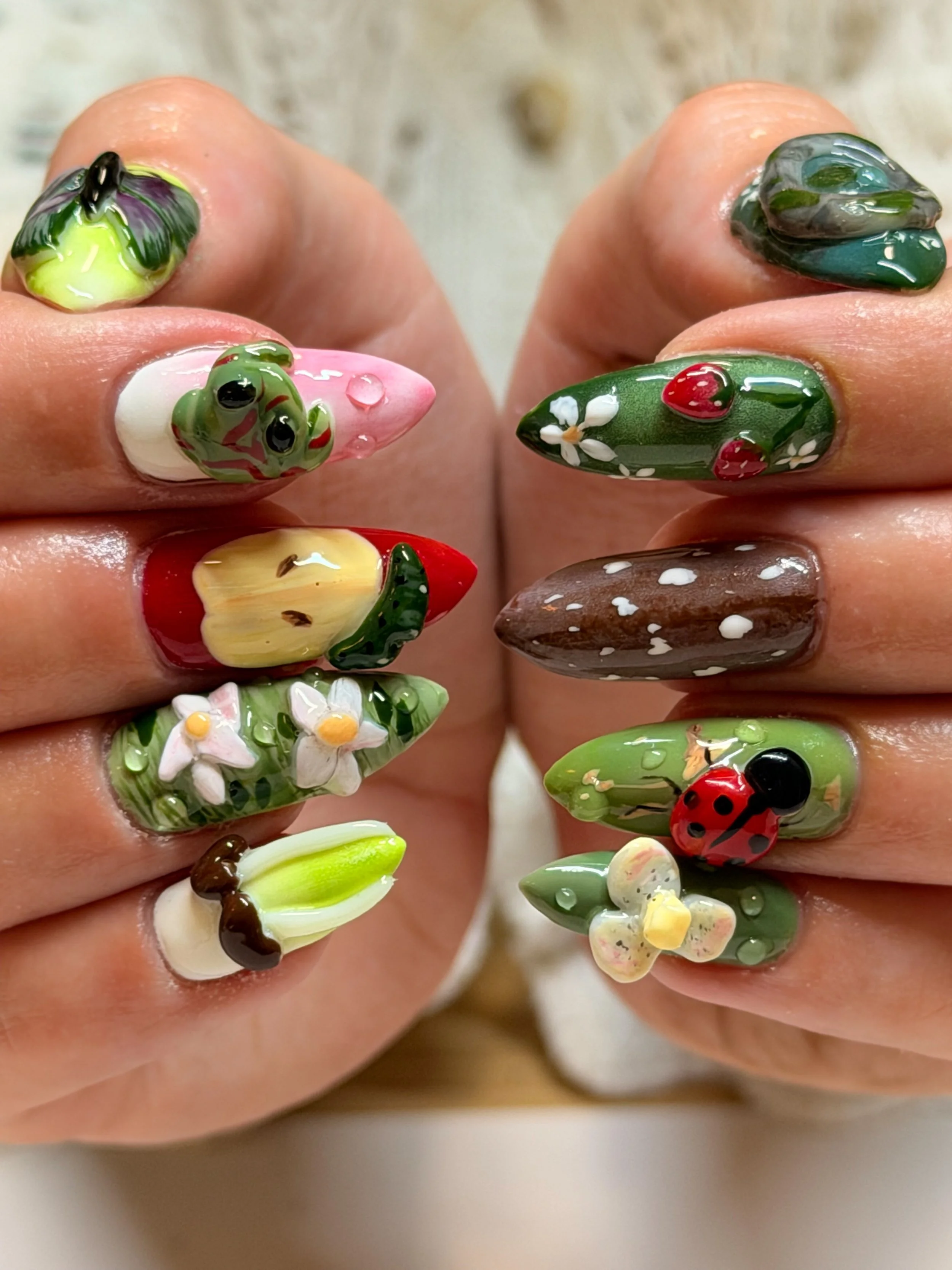 Close-up of hands with colorful, nature-themed 3D nail art featuring flowers, ladybugs, frogs, and other miniature designs.