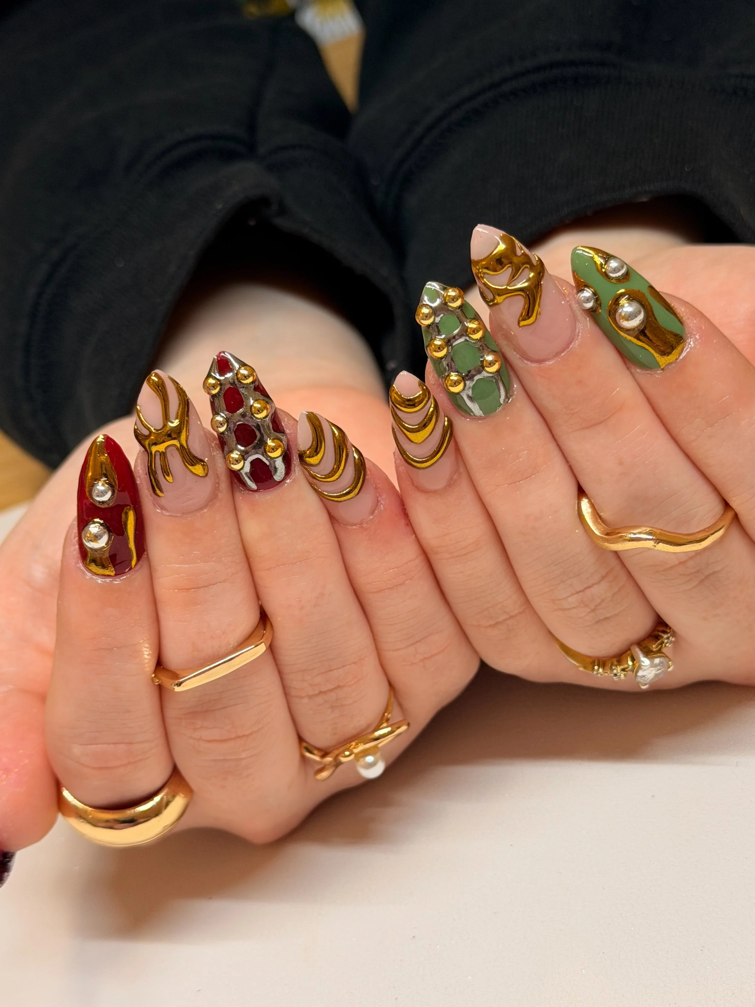 Close-up of a person's hands showing nail art with various colors and gold accents, adorned with rings.