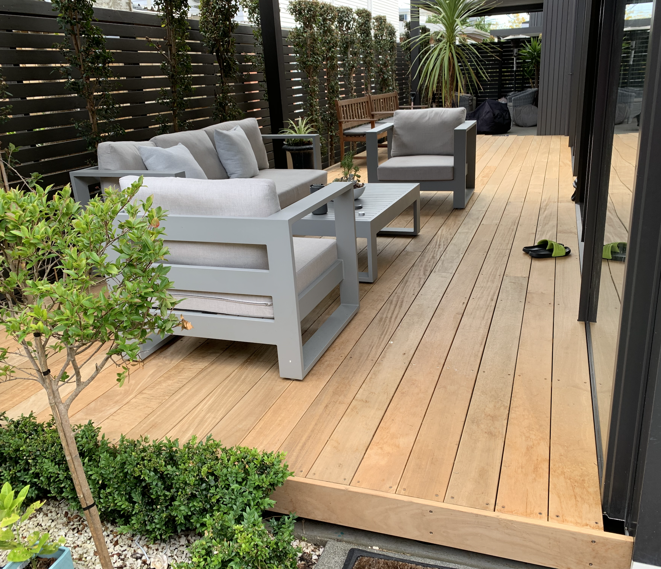 A modern outdoor wooden deck, enclosed by black slat fencing.
