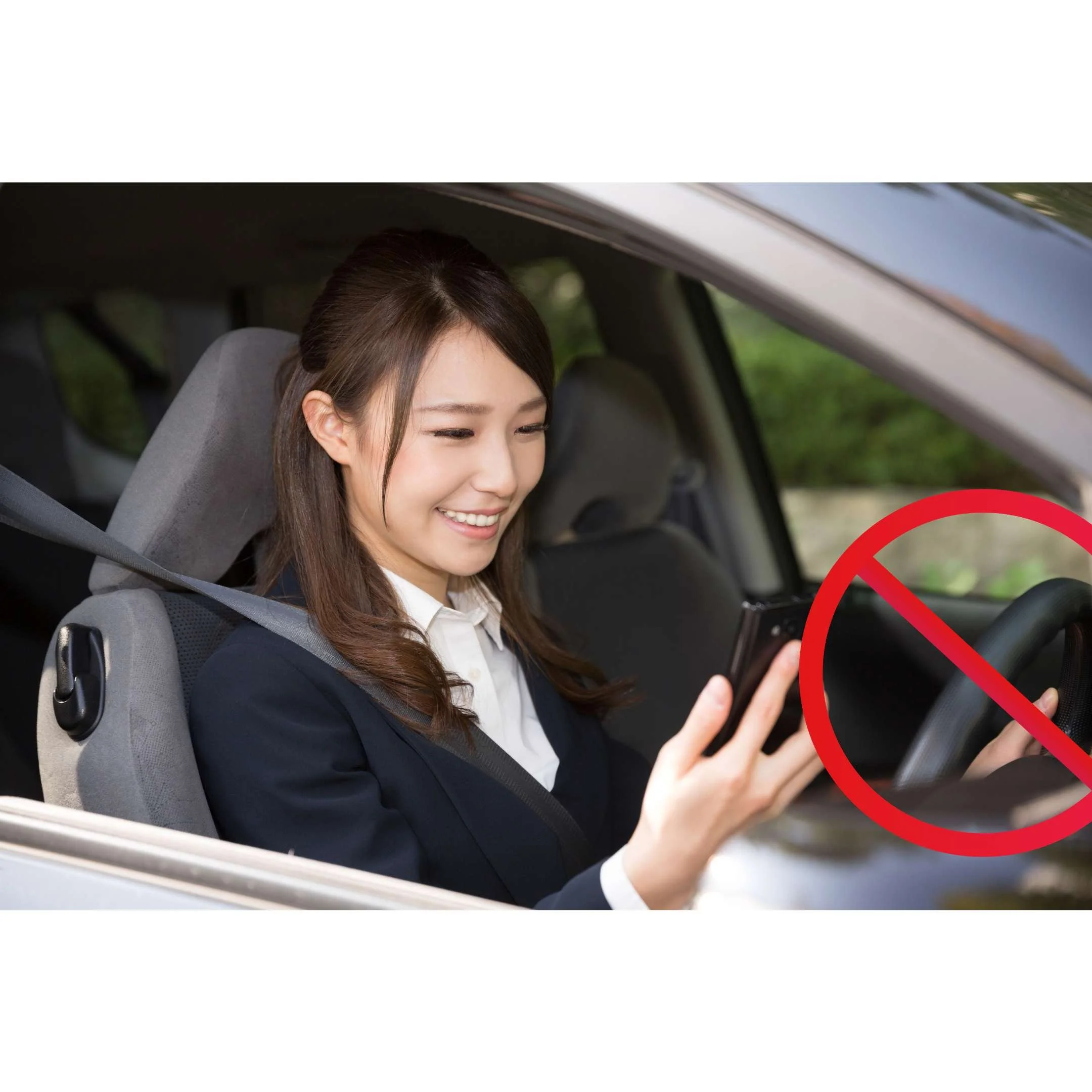 A woman with dark hair smiling and looking at her phone while seated in a car, with a red circle and line over part of the image indicating 'no' or prohibition.