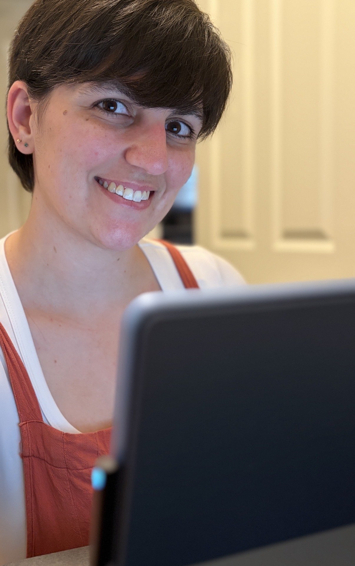 Kirsten Dantin LPC Headshot. A woman with short dark hair and earrings smiling as she looks at a laptop.