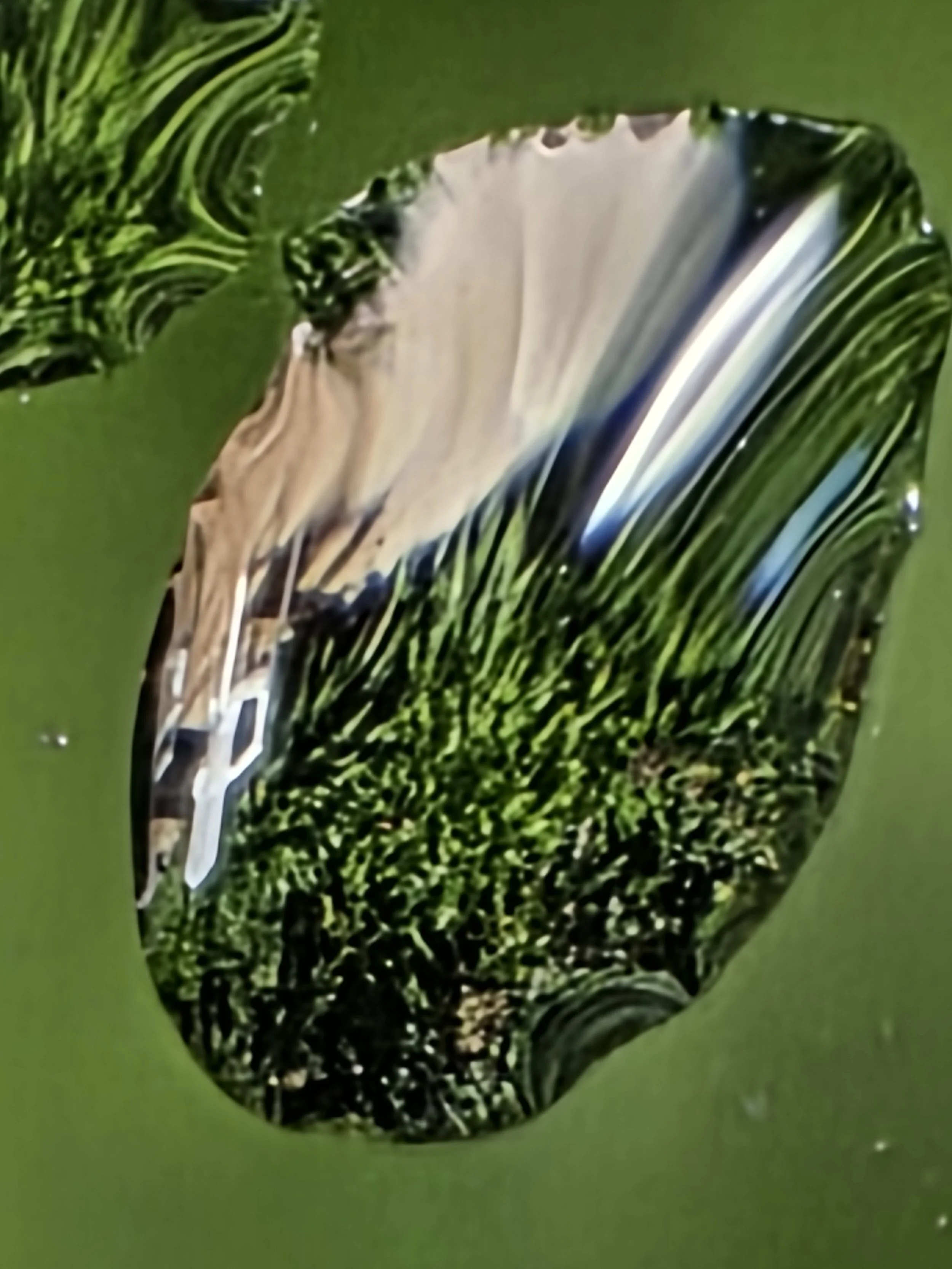 Close-up of a glass marble with swirling patterns of green, brown, and white, set against a green background.