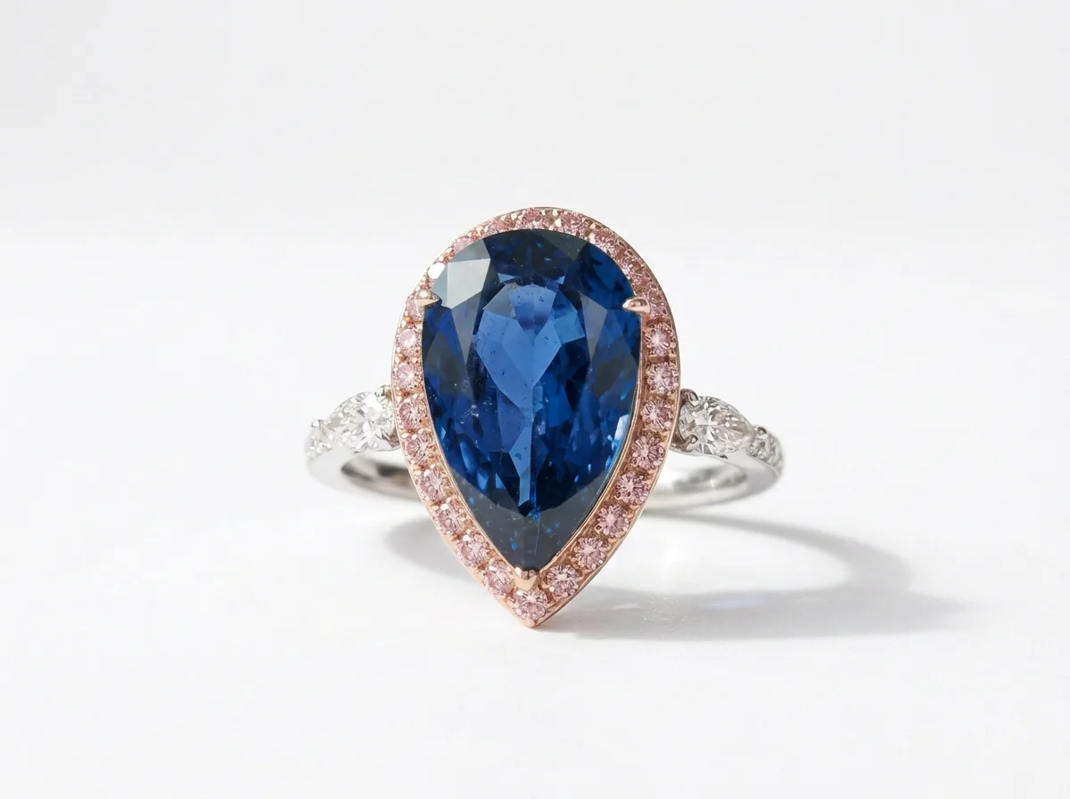 A ring with a large pear-shaped deep blue gemstone surrounded by a halo of small pink stones, set in a silver band with additional smaller stones.