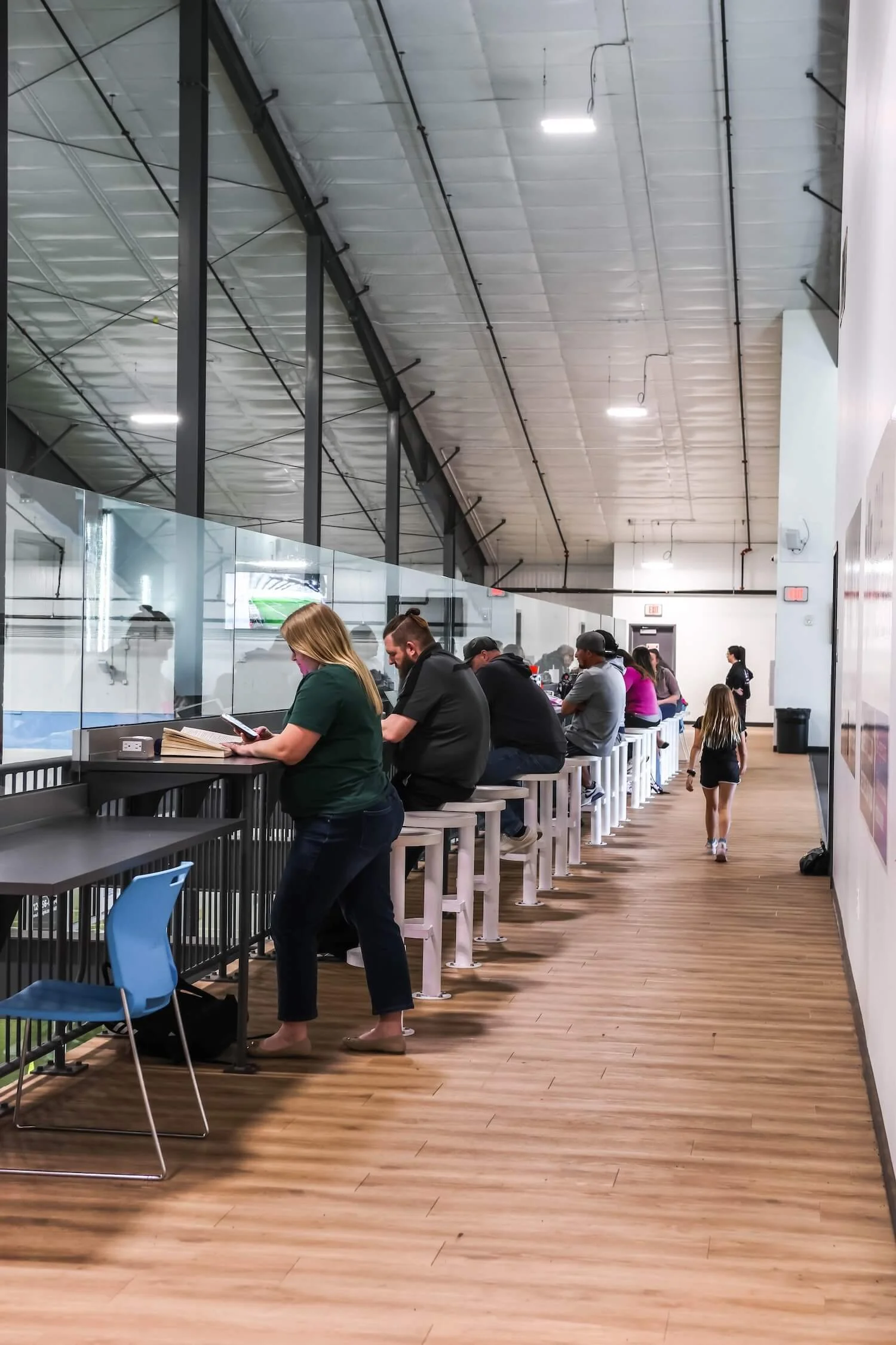People sitting on bar stools at a counter inside a sports bar, watching a game on TVs, with some children walking by.