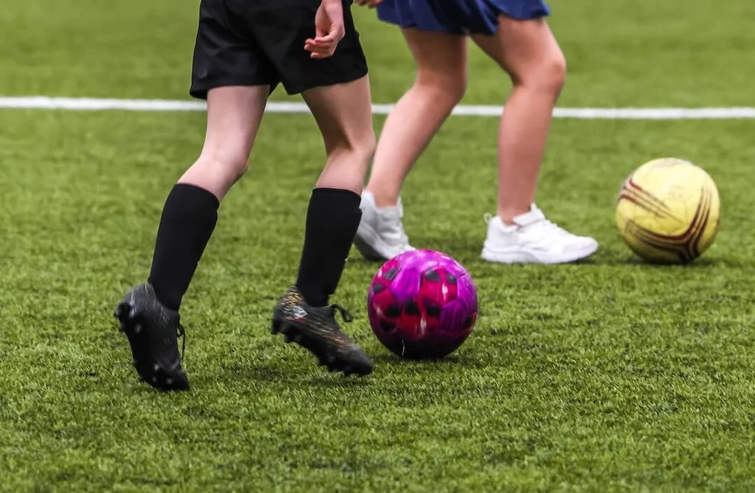Children playing soccer on a field with colorful soccer balls.